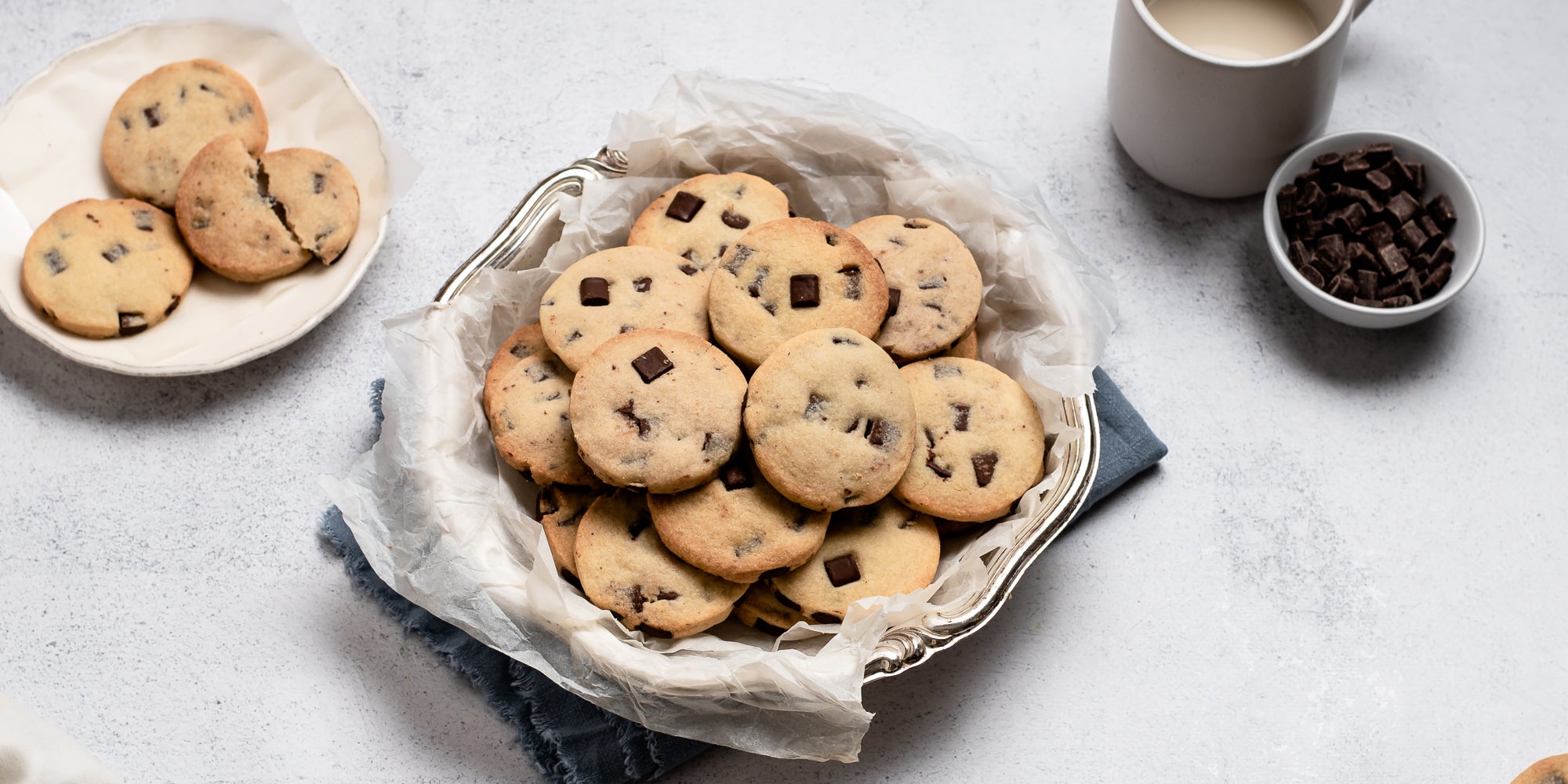 A cookie tin of Chocolate Chunk Shortbread biscuits, next to a small bowl of chocolate chunks