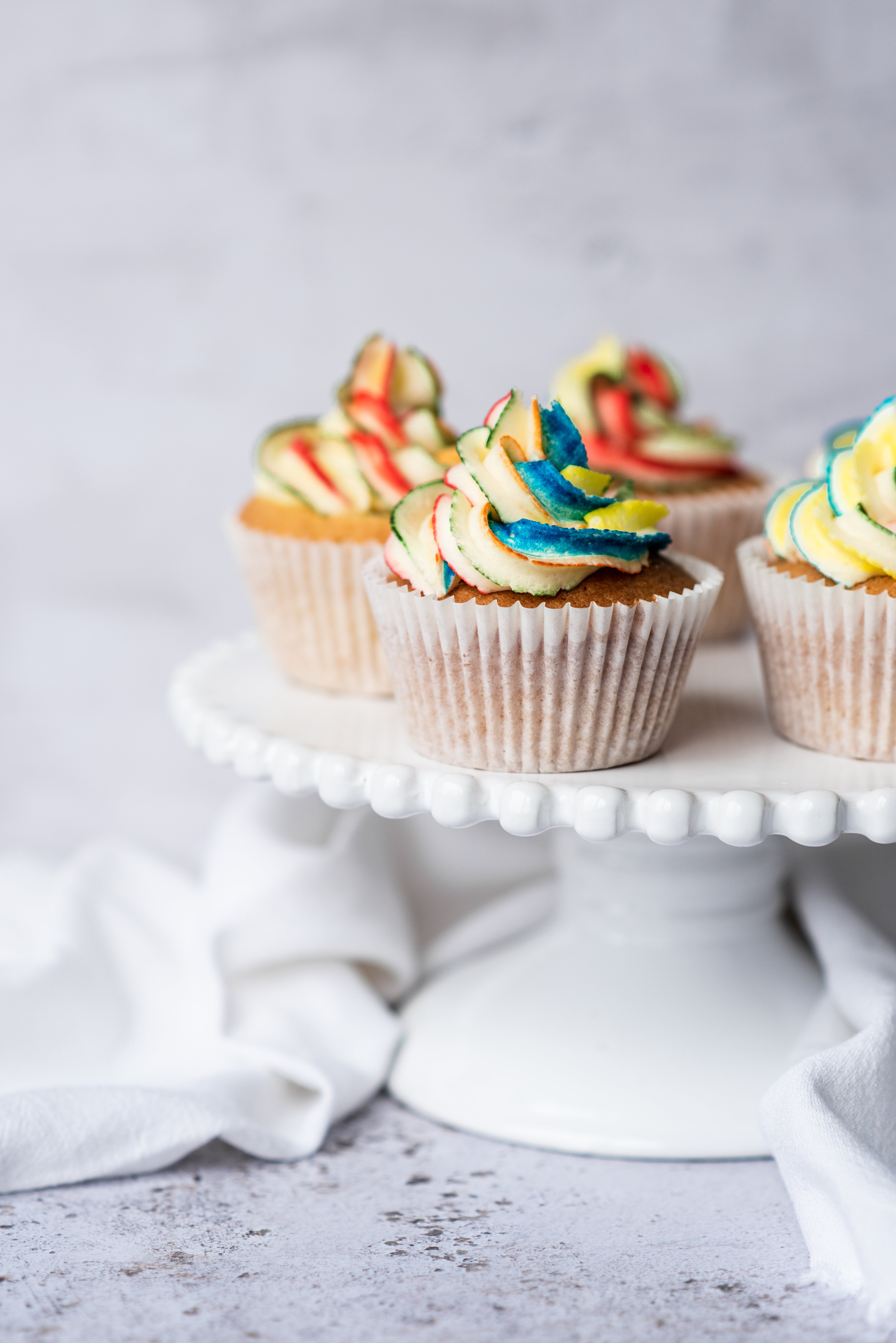 rainbow buttercream on a cupcake sitting on a cake stand