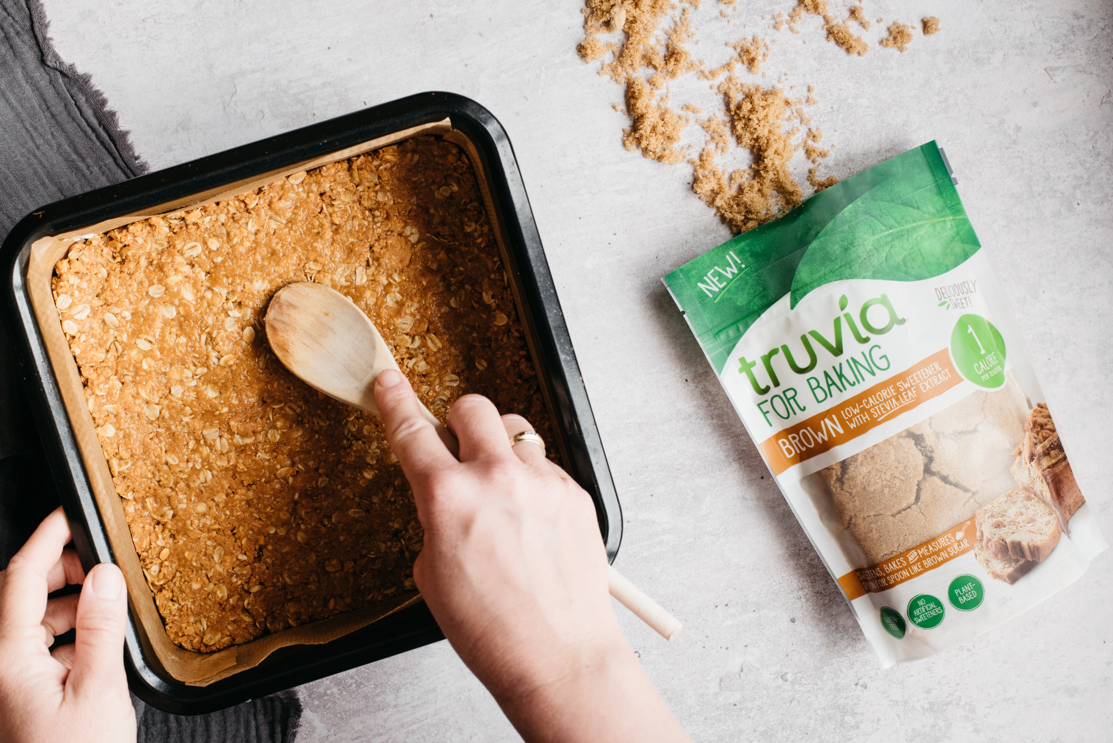 Base of Chocolate Peanut Butter Squares being pushed down with a wooden spoon, next to a bag of Truvia for Baking Brown