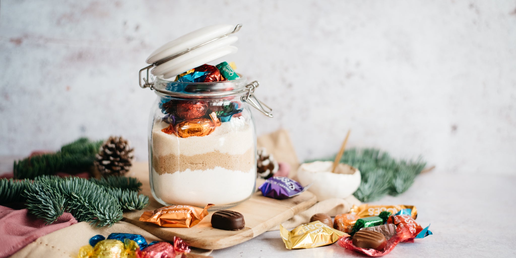 Christmas Cookies in a Jar with quality street surrounding the jar, on a board with pine cones 