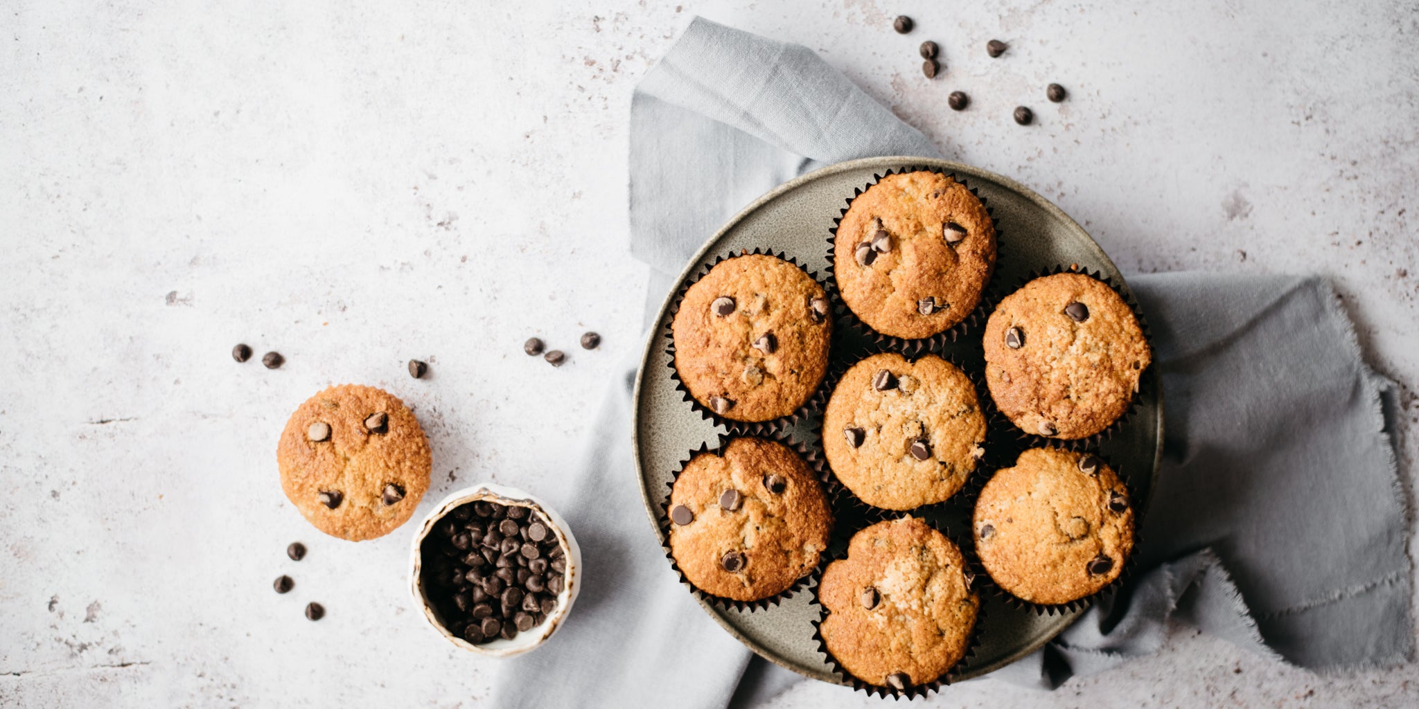 Top view of Wholemeal Banana & Chocolate Chip Muffins on a wire rack, next to a bowl of chocolate chips