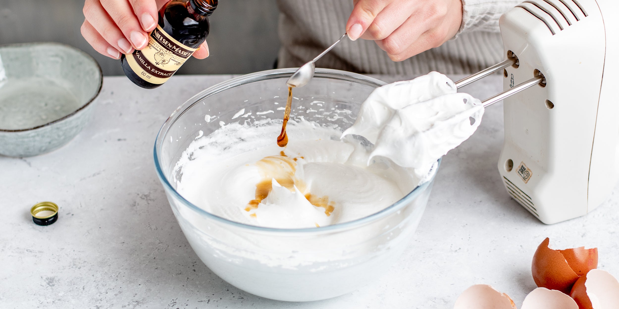 Meringues mid-whisk adding a generous drizzle of Nielsen-Massey Vanilla extract to the mixture