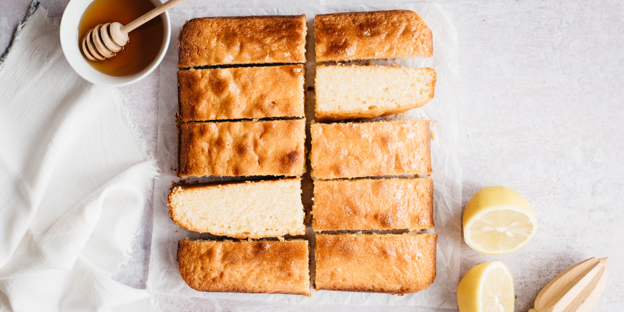 Overhead shot of Lemon Drizzle traybake with a small bowl of honey and some sliced lemon