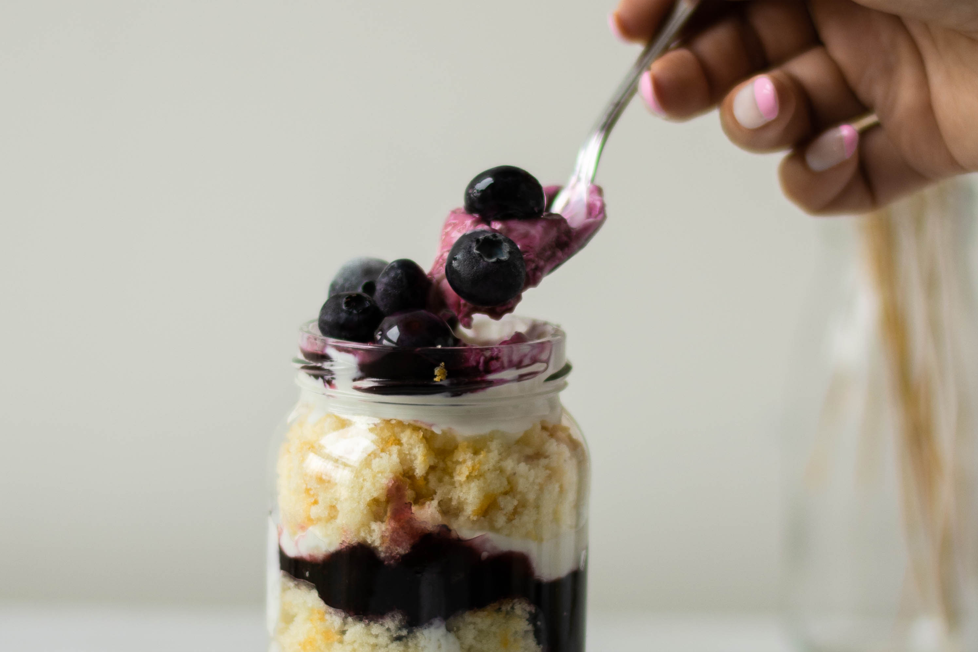 Close up of the top of a Lemon & Blueberry Cake Jar, with a spoonful dipping in to a dollop of blueberry yoghurt