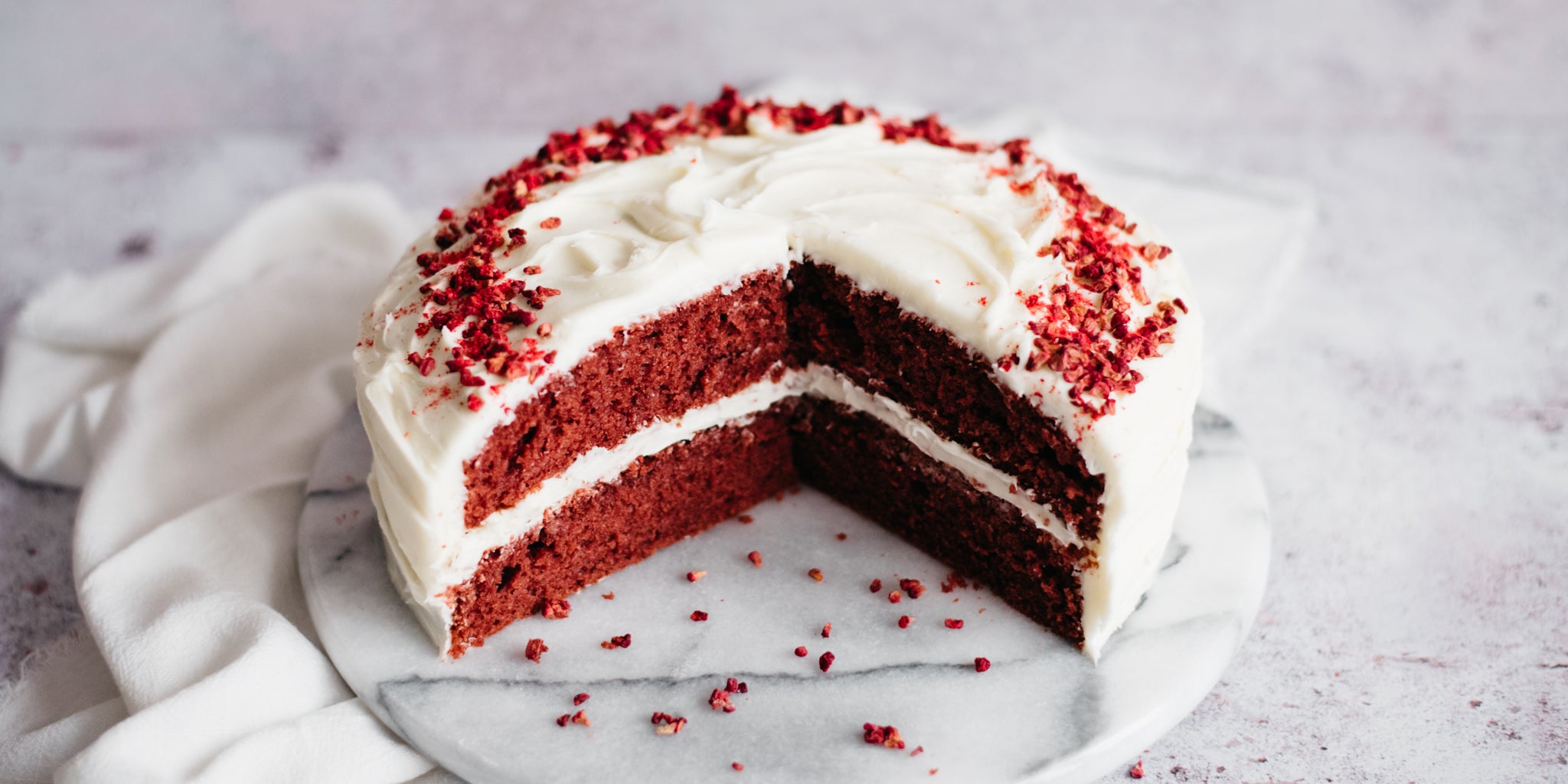Red Velvet Cake with slices cut out of it, showing the rich, red insides and Red Velvet Cake crumbs on the cake board