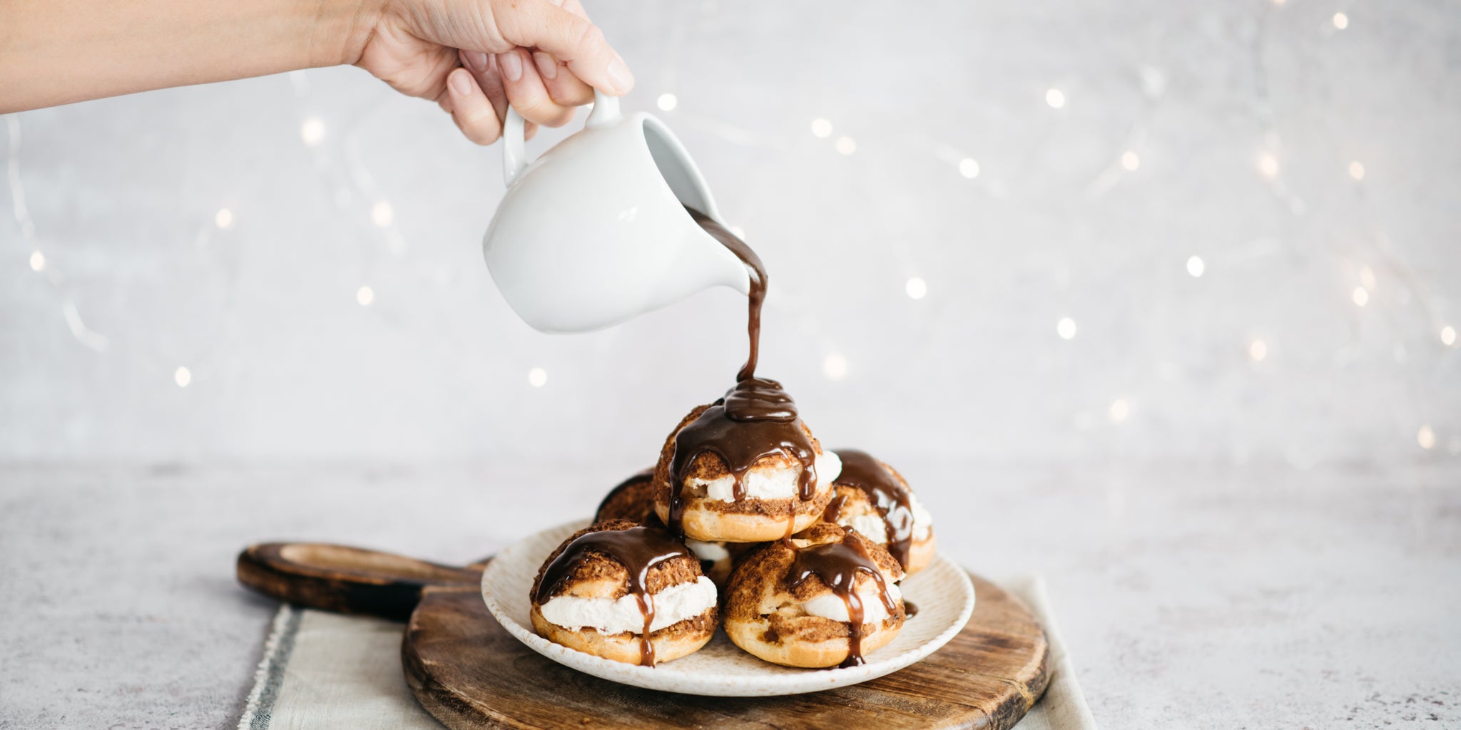 Hand pouring a jug of toffee sauce over a plate of profiteroles