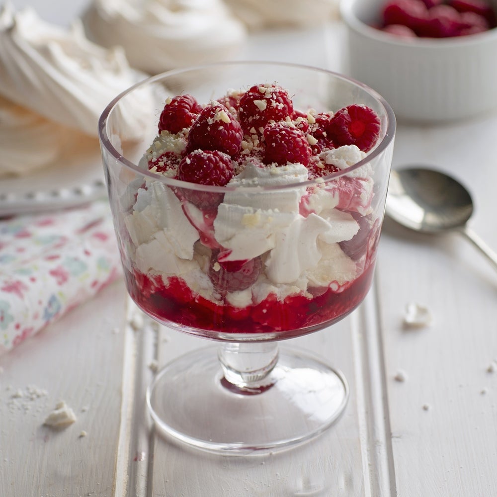 Layered Eton Mess with strawberries, raspberries, meringue and double cream in a glass dessert bowl