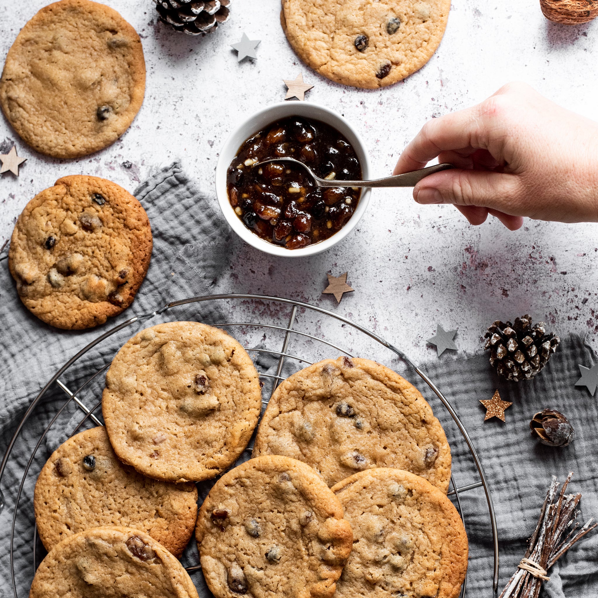 Mince pie cookies on a circular cooling rack, a hand spooning mincemeat out of a small bowl