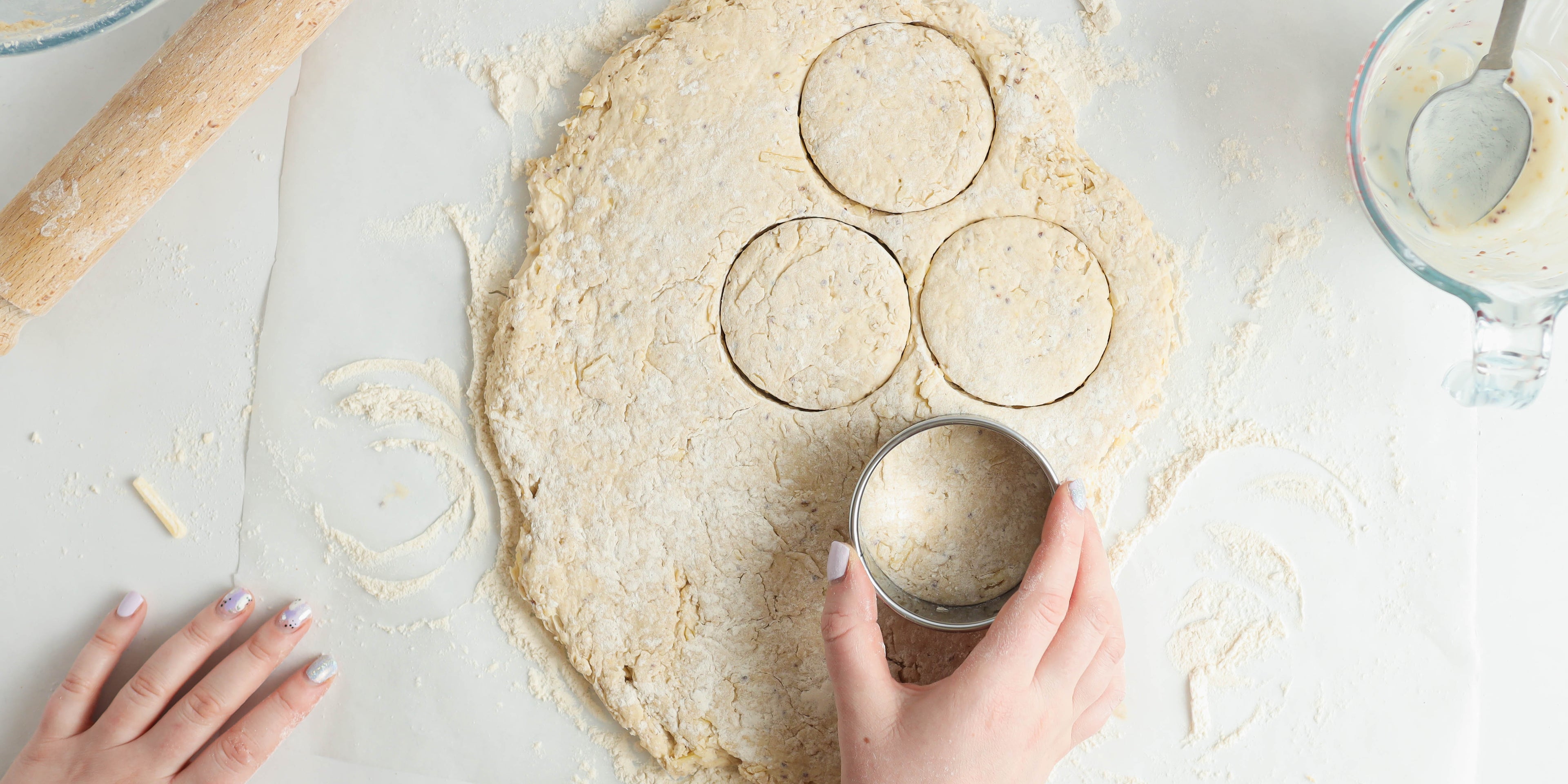 Top view of Cheese Scones dough being cut into circle shapes with hand holding cookie cutter ready to bake