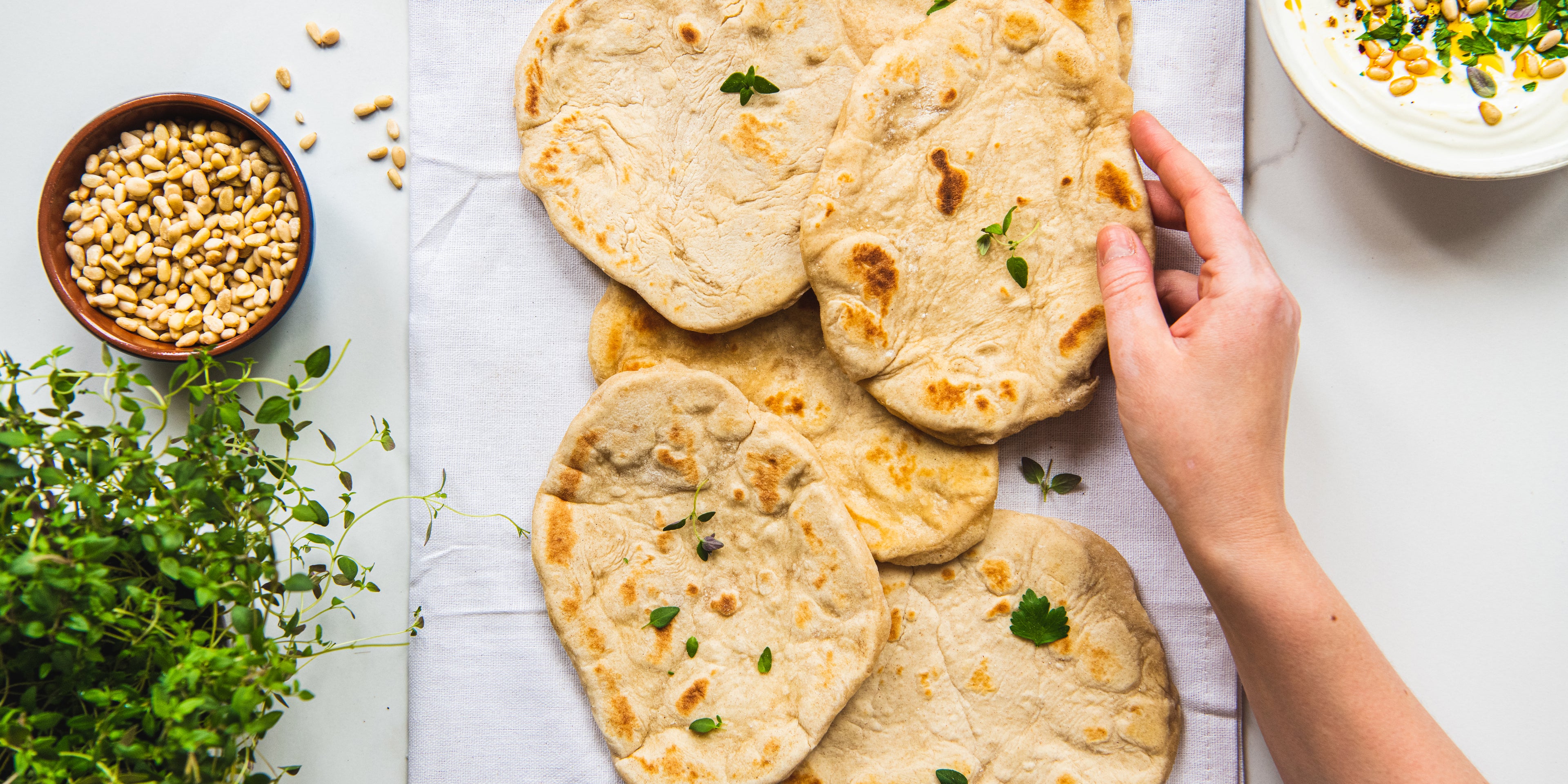 Top down shot of hand reaching in to pick up a kefir flatbread on a plate of kefir flatbreads