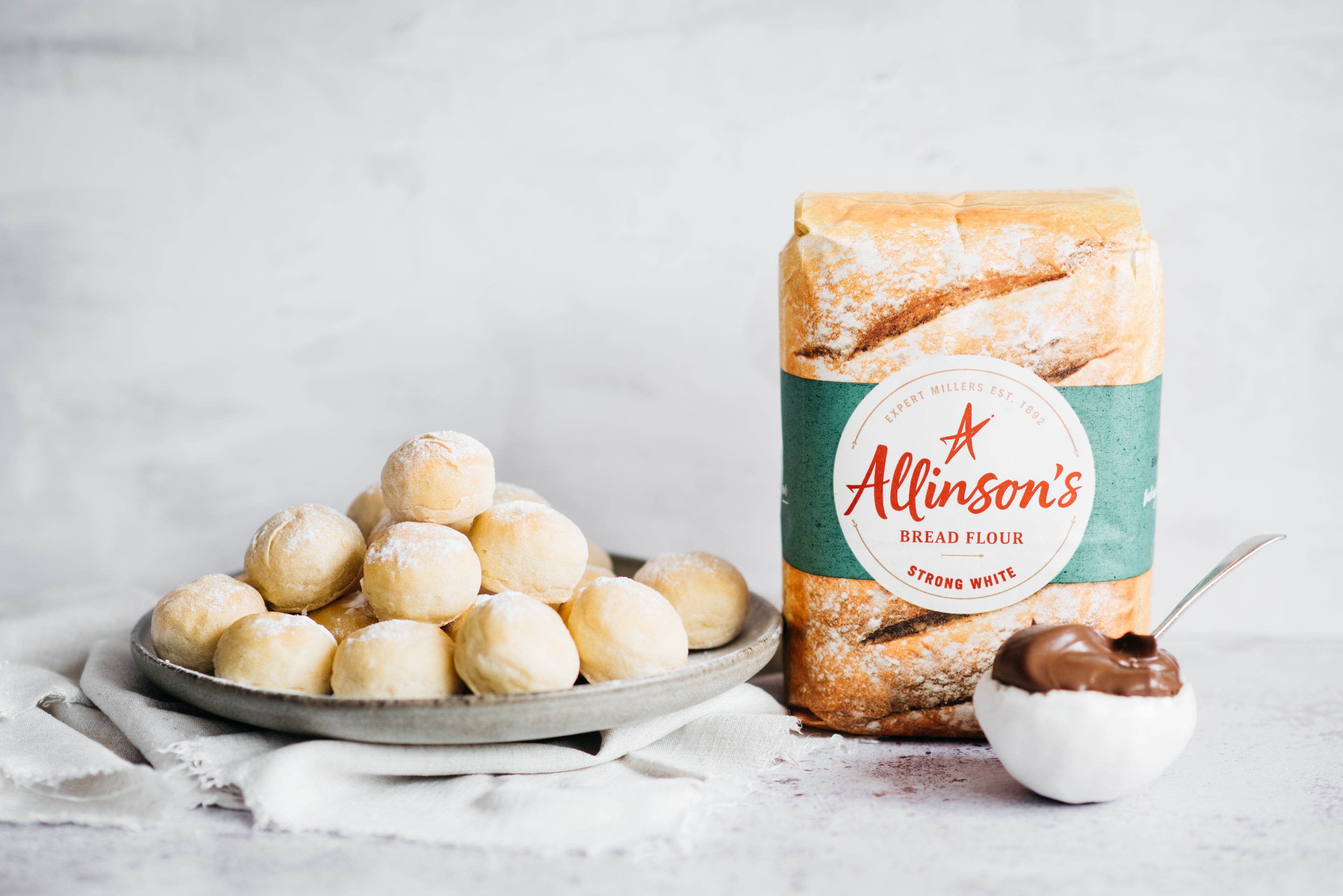 Chocolate Dough Balls on a plate, next to a bag of Allinson's strong white flour, and a bowl of chocolate sauce with a spoon