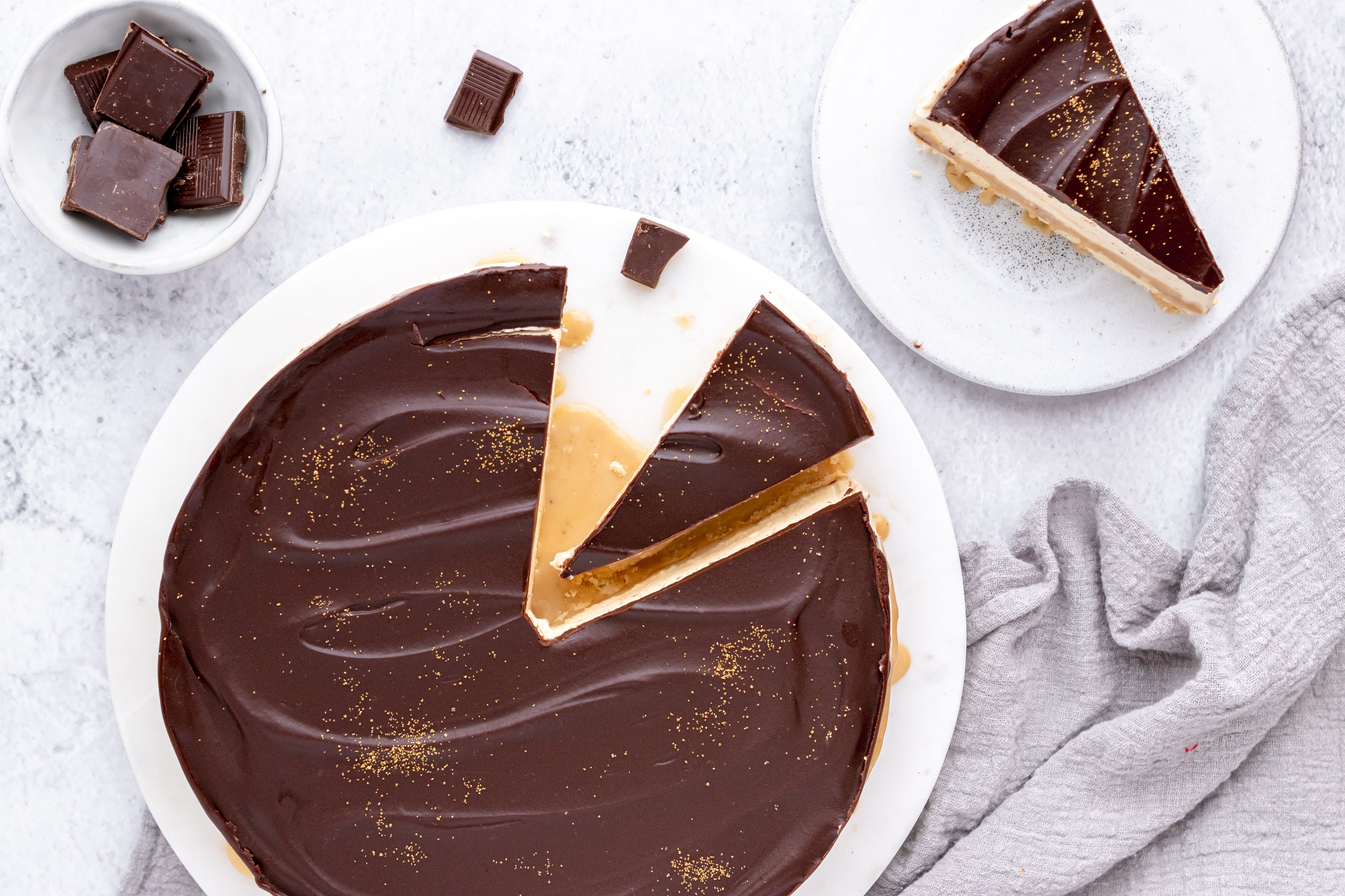 Millionaire's Cheesecake with a slice cut out, next to a small bowl of chocolate pieces