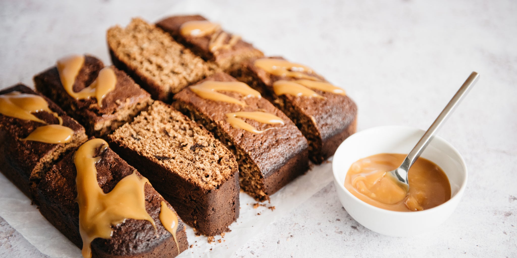 Close up of Ultimate Wholemeal Sticky Toffee Pudding sliced into squares, next to sticky toffee sauce to drizzle over the top