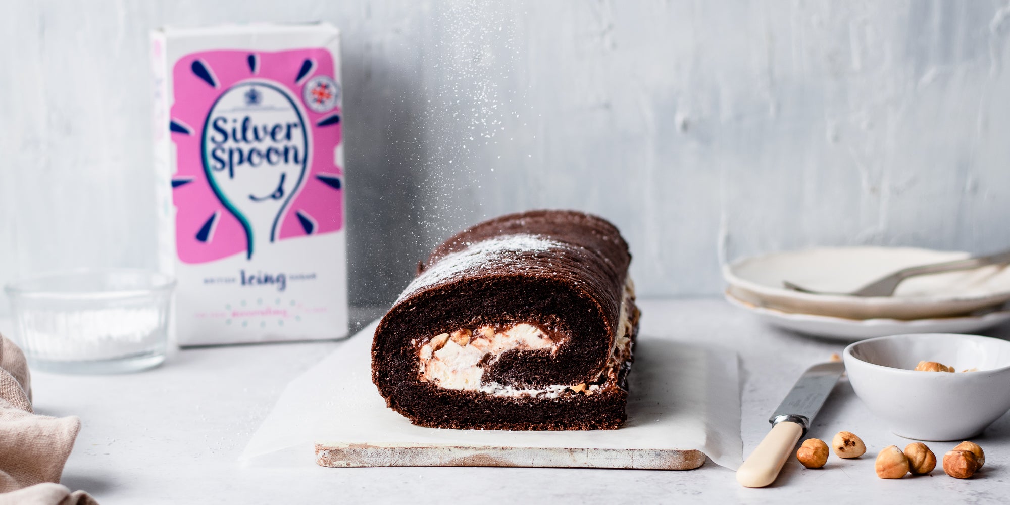 Chocolate Roulade with a box of Silver Spoon Icing Sugar in the background, next to a knife ready to serve, and hazelnuts