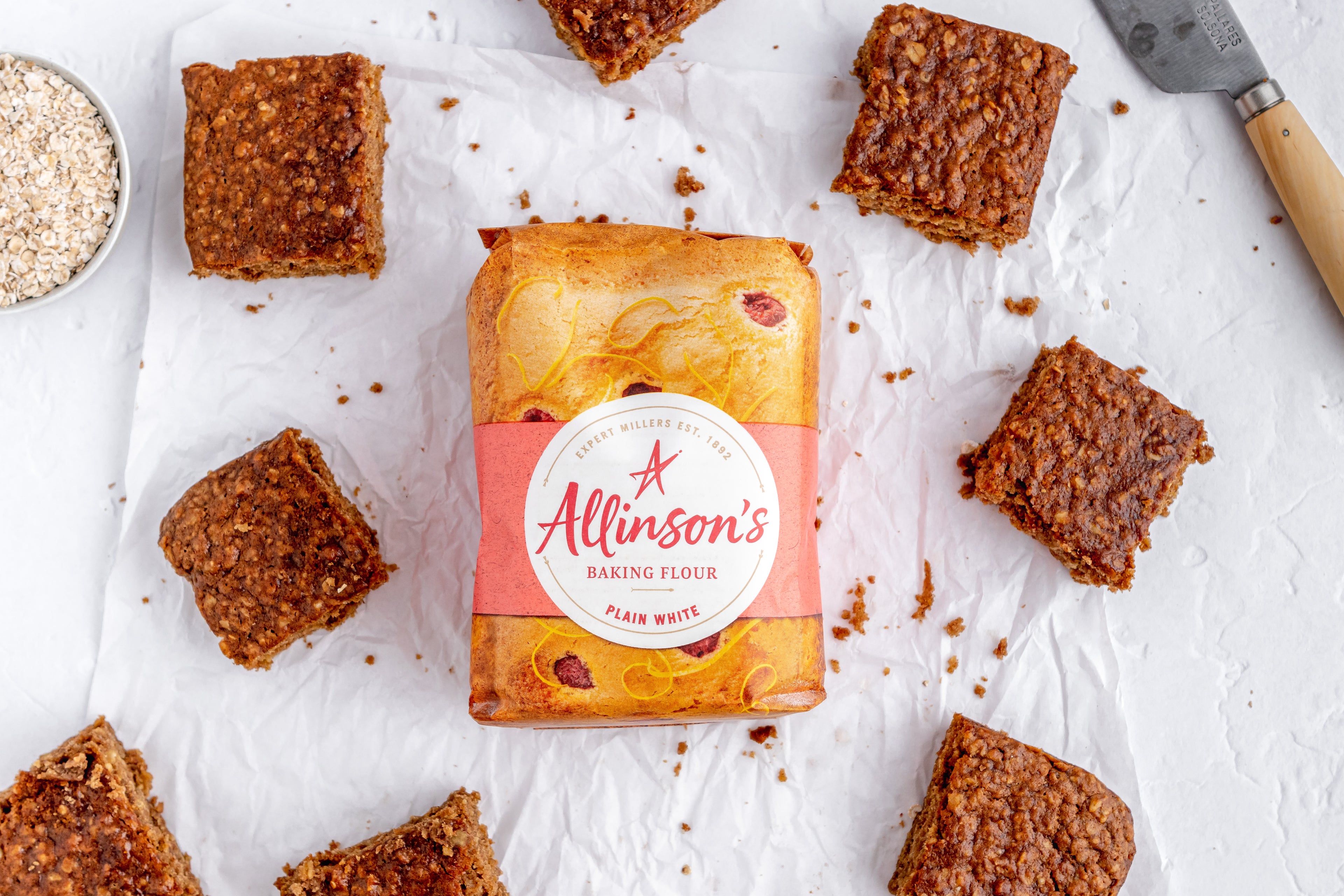 Square slices of Sticky Yorkshire Parkin placed around a bag of Allinson's Plain White Flour on baking paper