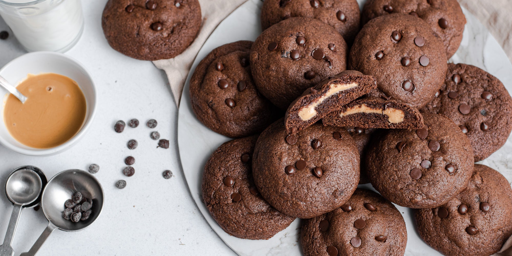 A batch of Chocolate & Peanut Butter Stuffed Cookies with a cookie sliced in half, showing the gooey insides.