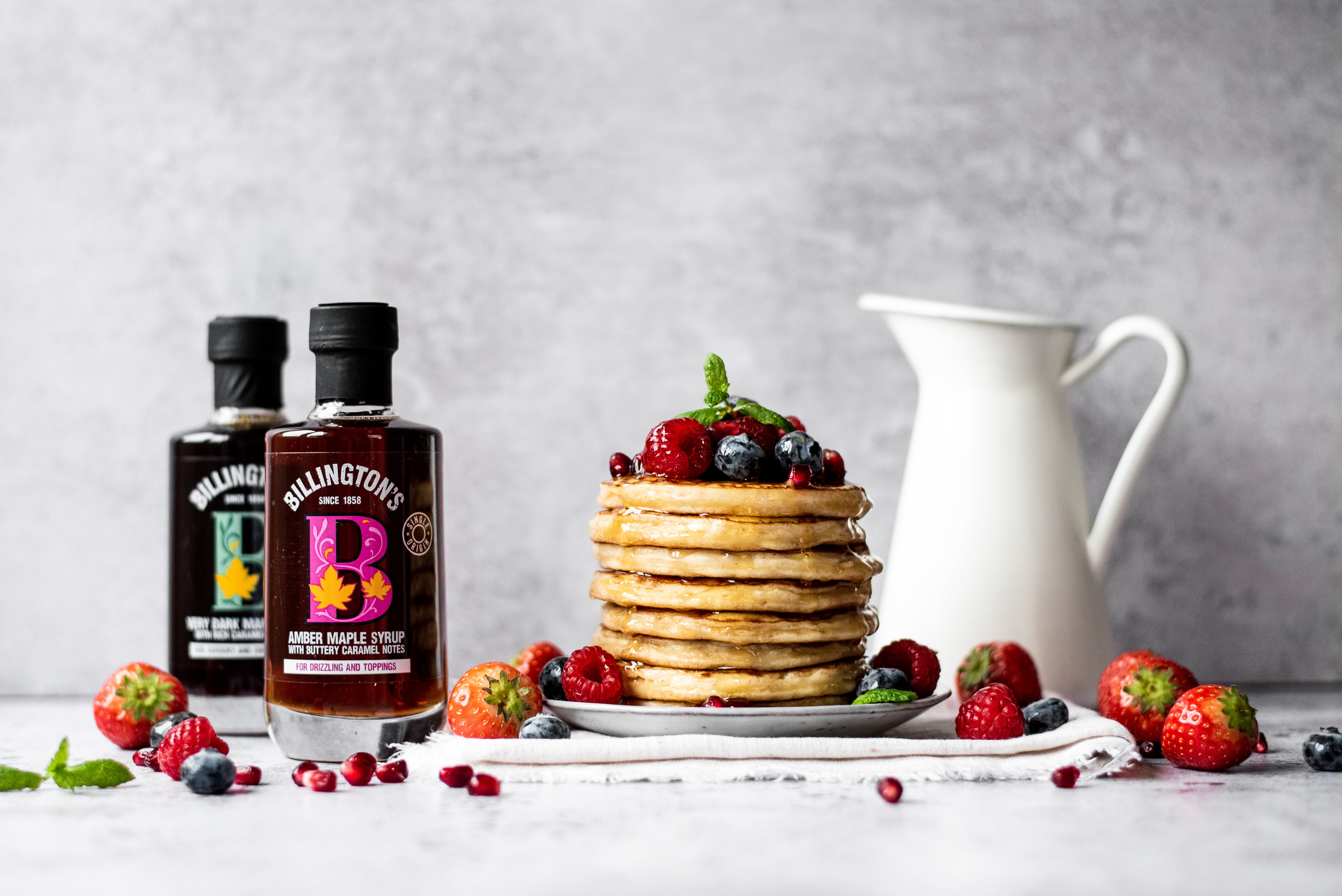 Stack of pancakes topped with berries and two jars of maple syrup
