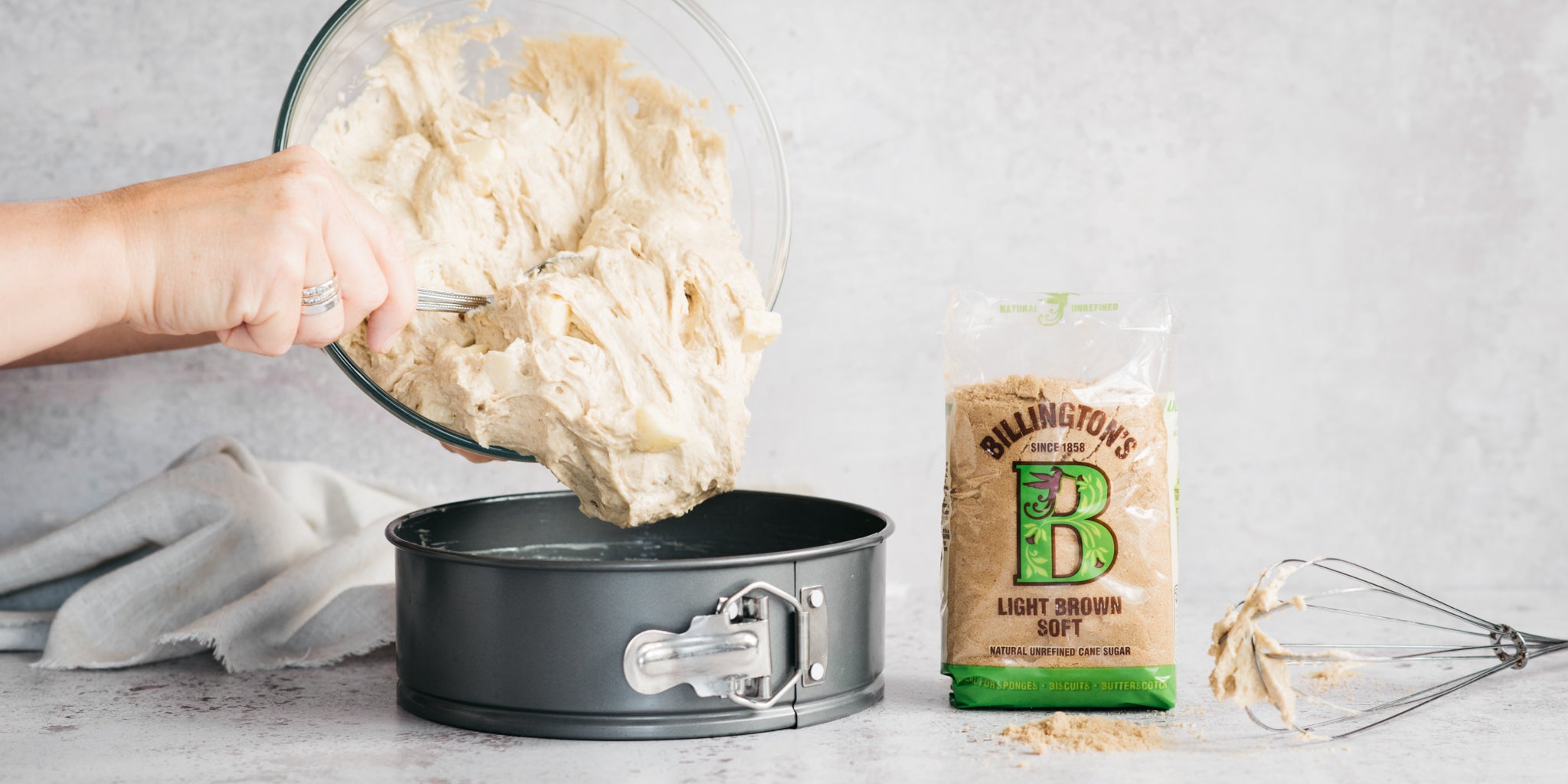 Cake mixture being poured into a cake tin beside a pack of sugar