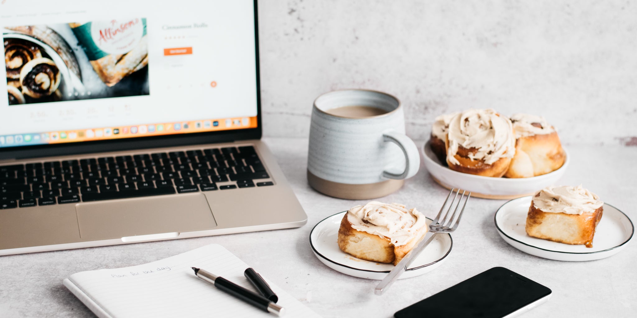 Cinnamon rolls on a plate with cup of coffee, laptop, phone and notepad