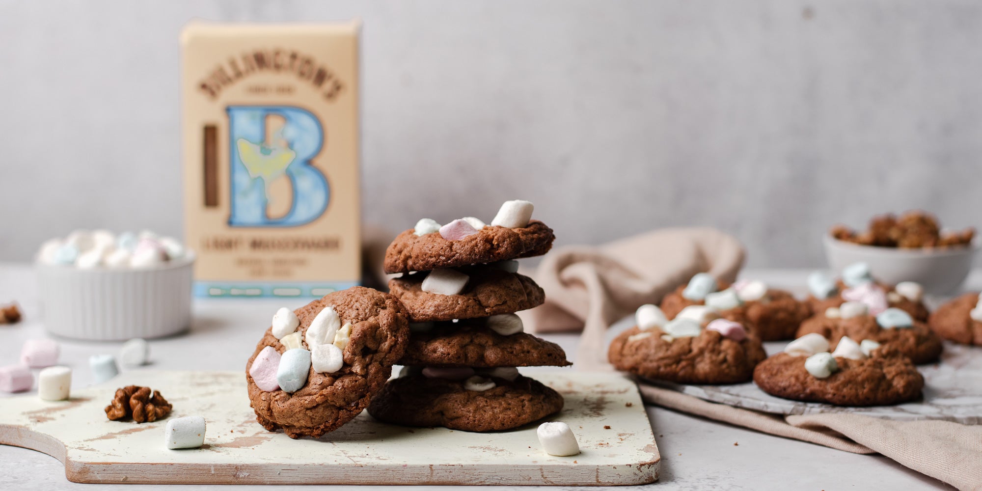 Rocky Road Cookies stacked on top of each other, on a serving board with a box of Billington's Light Muscovado in the background