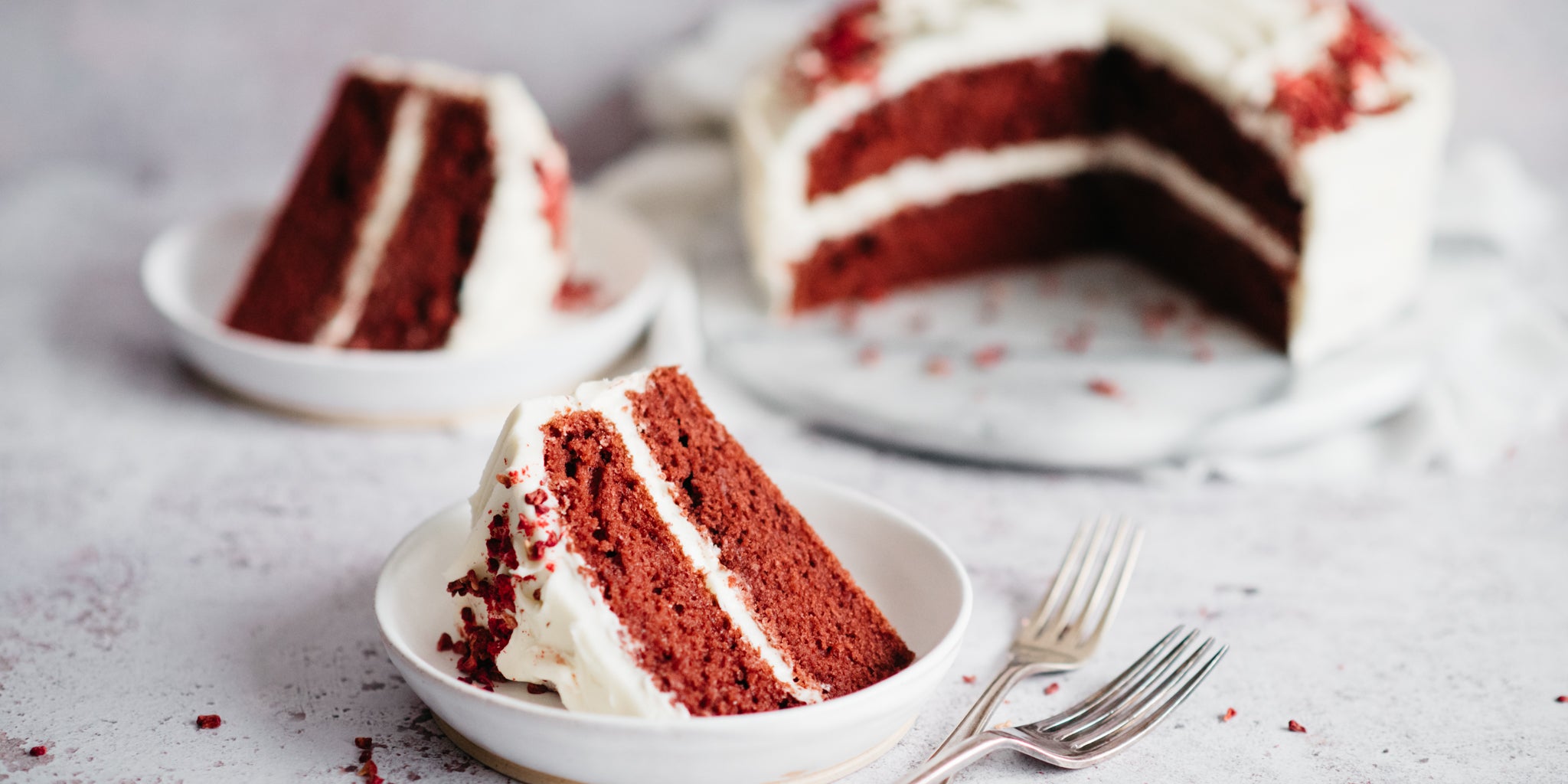 Close up of a slice of Red Velvet Cake served on a plate, showing the rich red insides of the cake