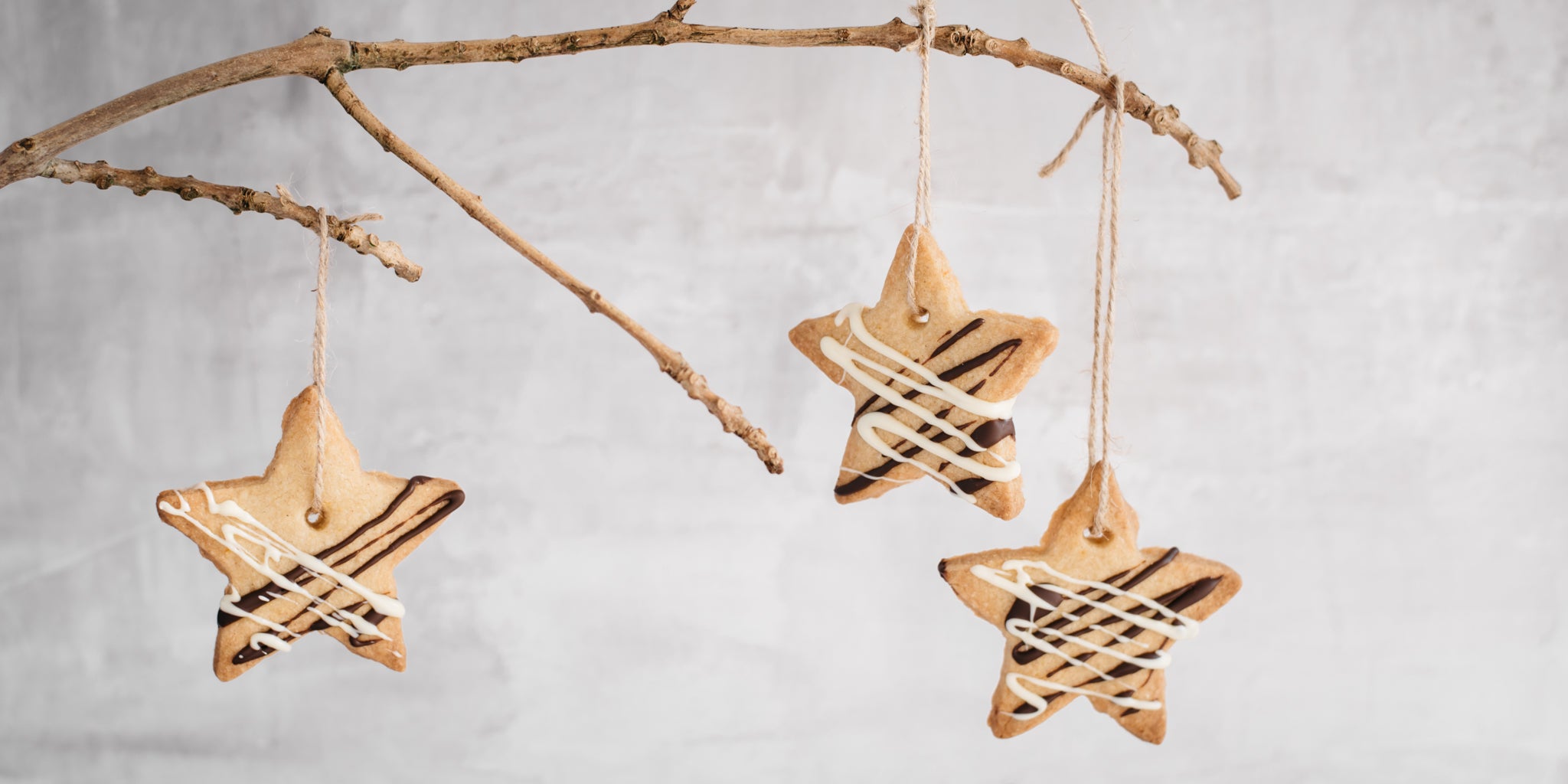 Orange & Ginger shortbread stars hanging from a branch with twine threaded through them.