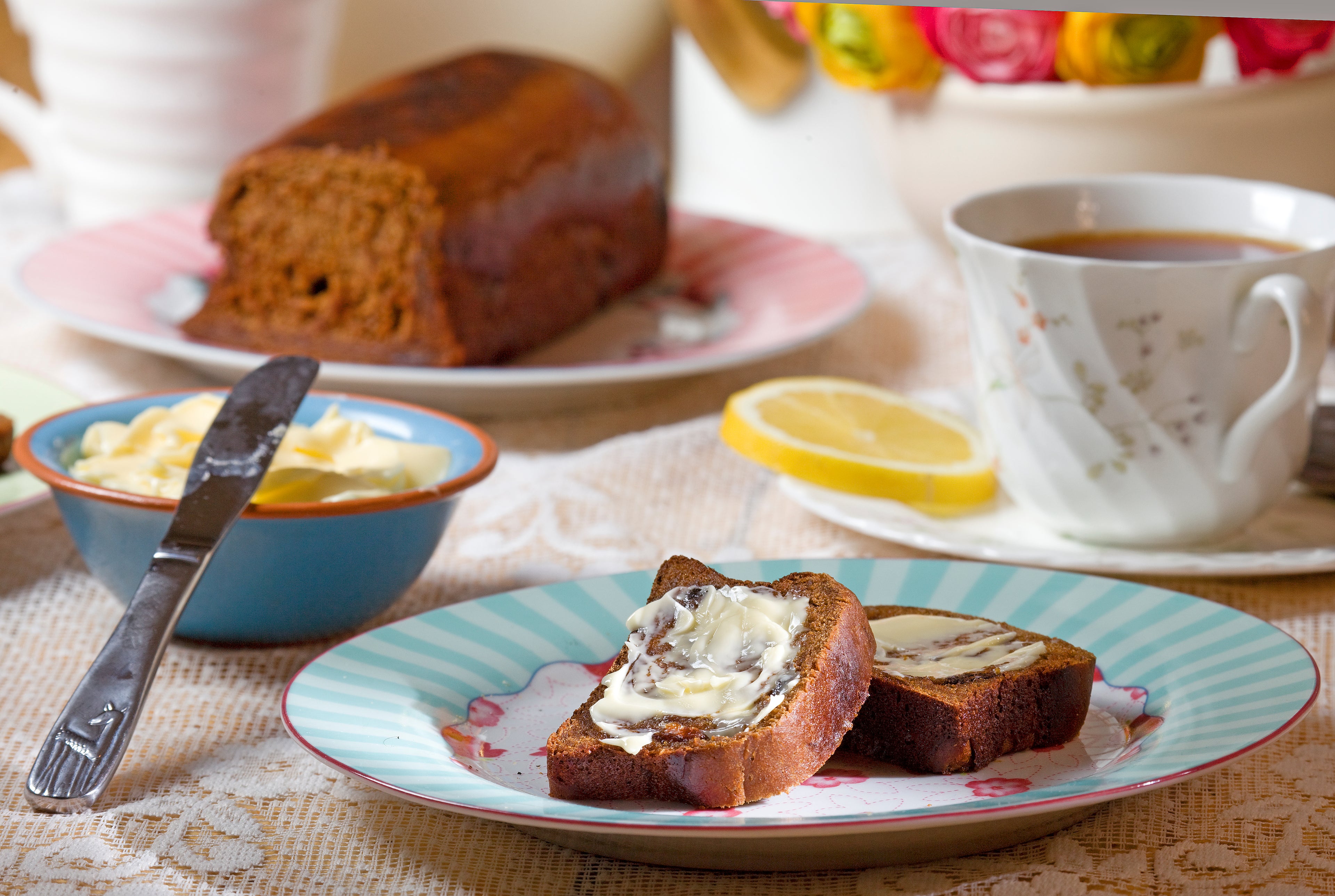 Slices of homemade malt loaf covered with butter on a blue and white plate