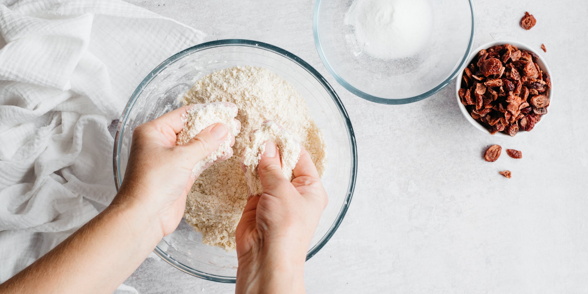 Hands rubbing together flour and butter in a glass mixing bowl with bowl of cranberries beside