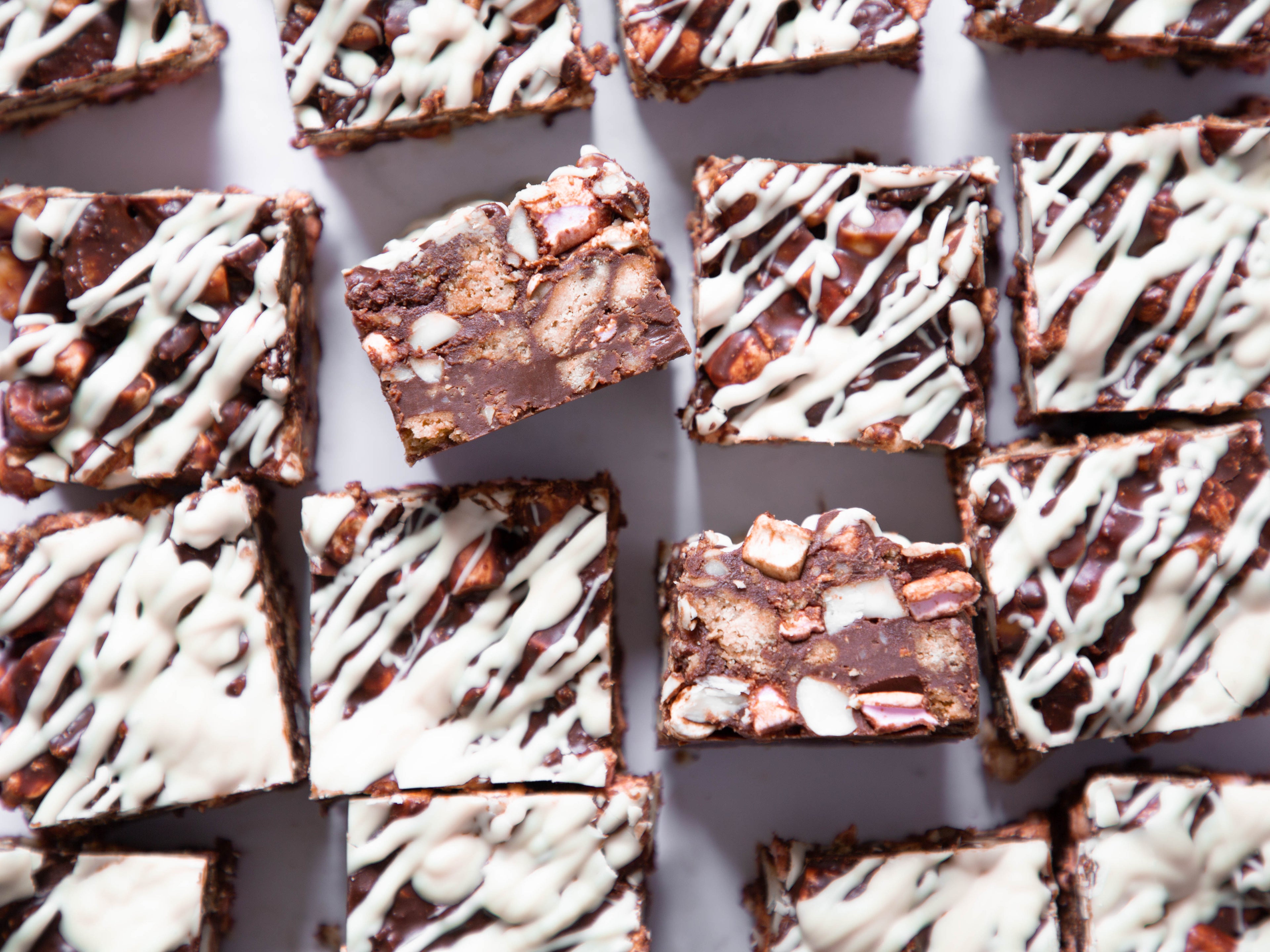 Close up shot of square of rocky road, some drizzled with white chocolate and two squares turned on their sides to showing filling