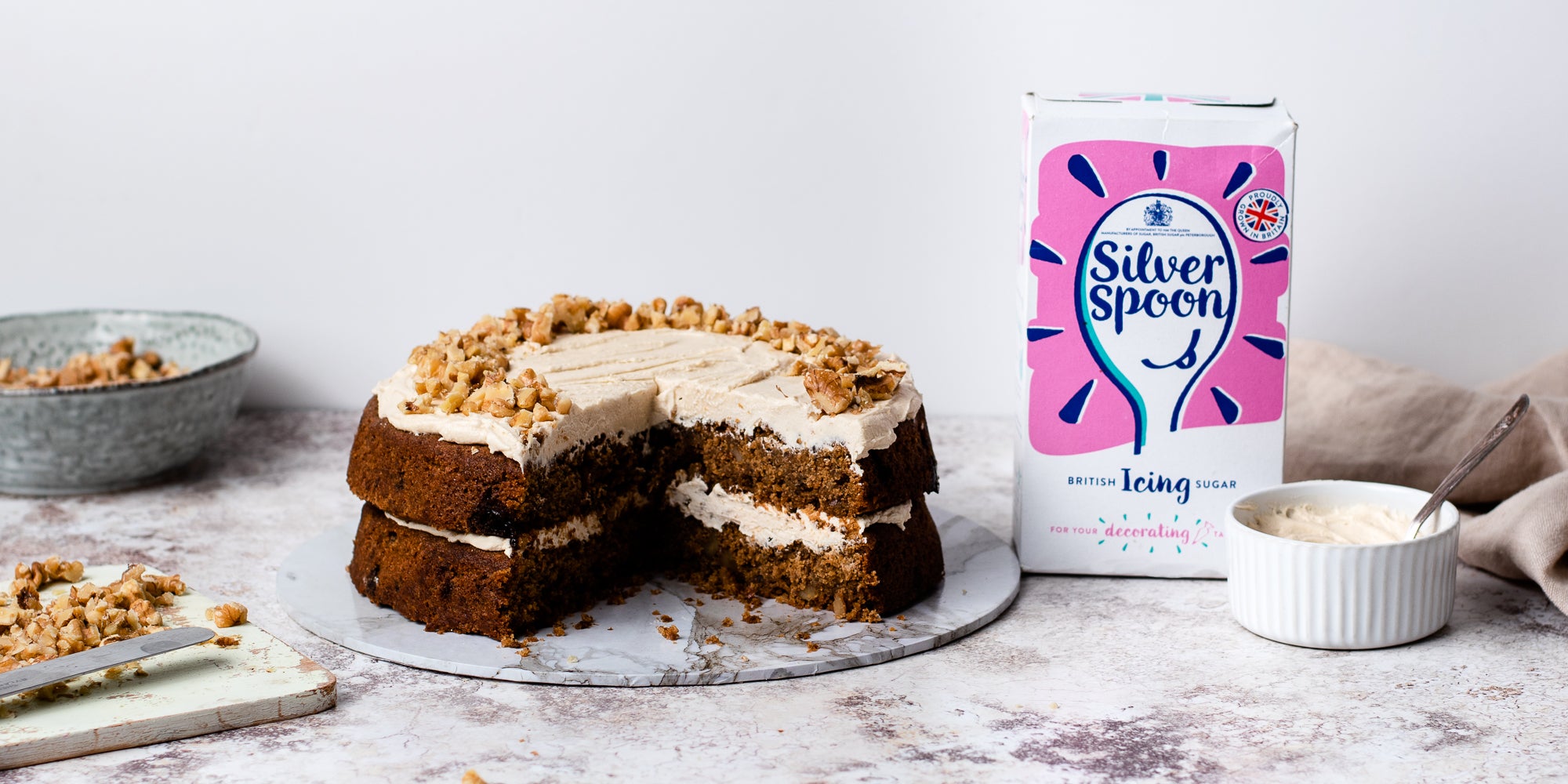 Gluten Free Vegan Coffee Cake on a cake board with a slice cut out, next to a box of silver spoon icing sugar