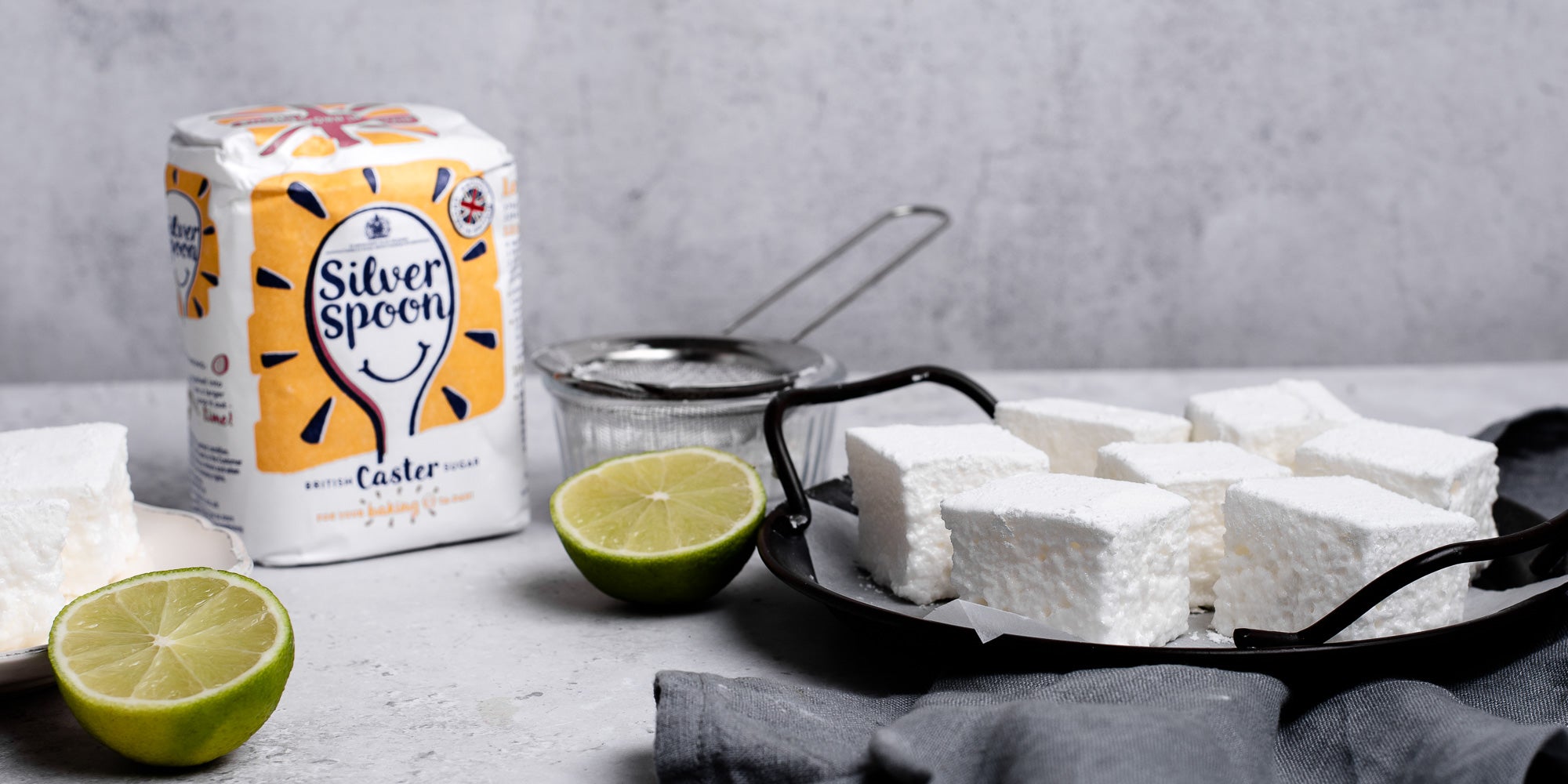 Gin & Tonic Marshmallows next to a bag of Silver Spoon Caster Sugar and sliced lime