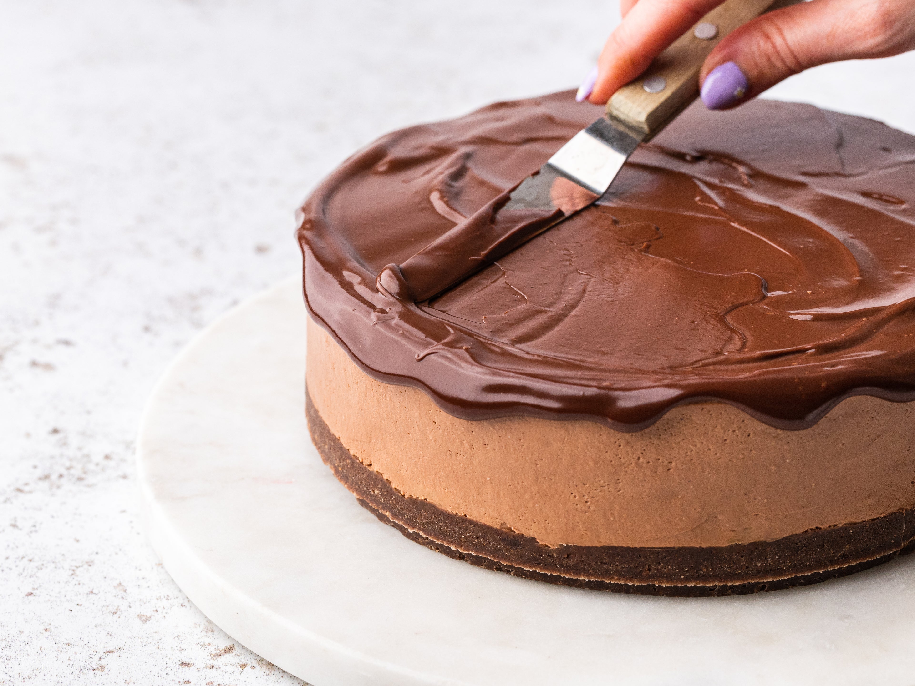 Chocolate ganache being spread on top of a cheesecake 