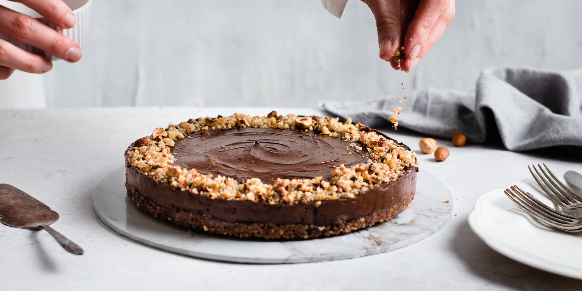 Raw Chocolate Avocado Cheesecake being hand finished with a hand scattering chopped nuts around the edge of the cheesecake