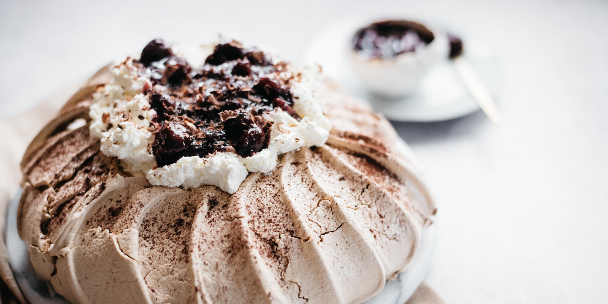 Close up of Black Forest Pavlova with a bowl of cherry kirsch in the background