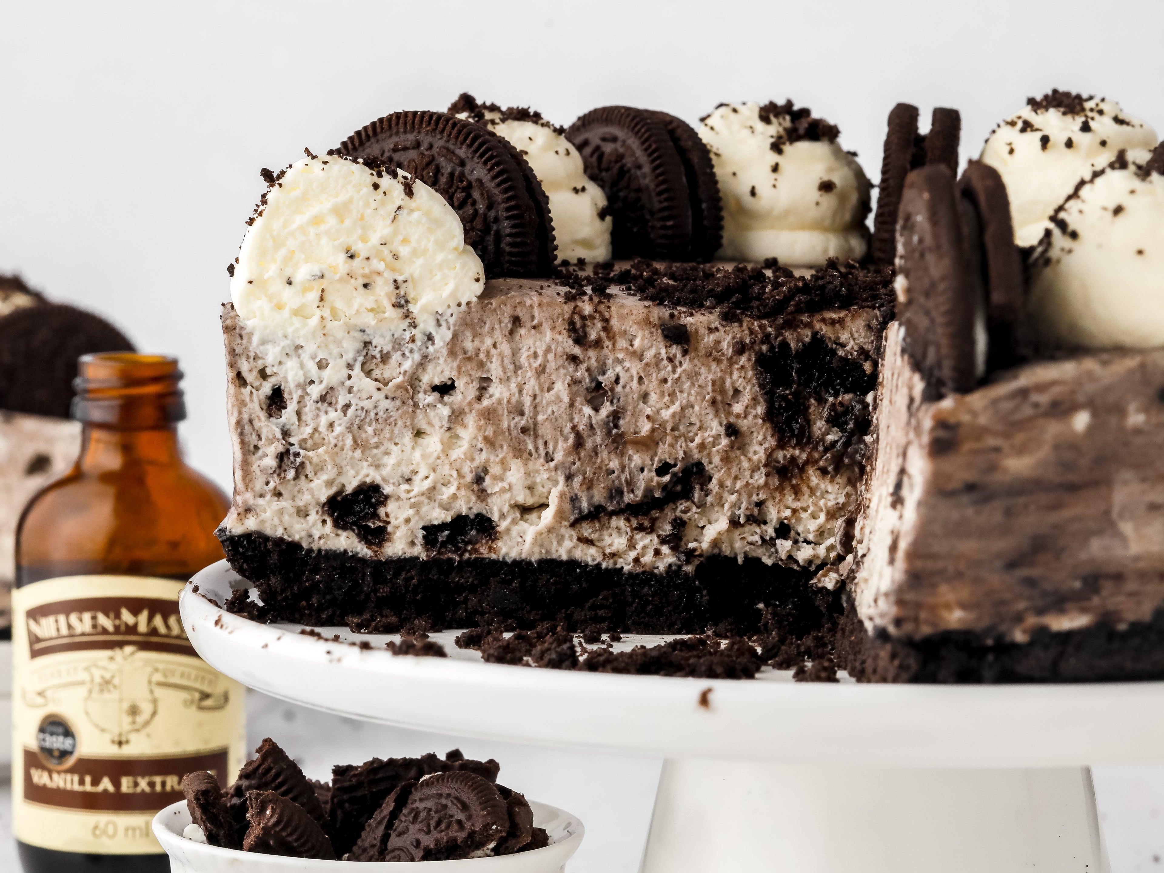 Oreo cheesecake on a cake stand with vanilla bottle beside it