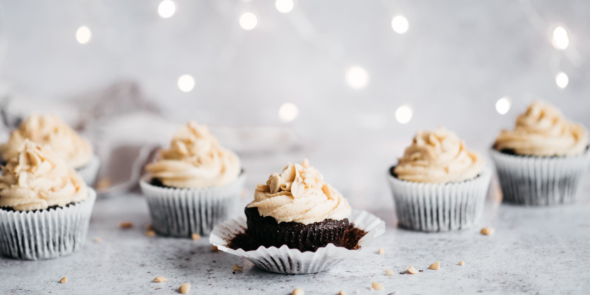 Row of chocolate muffins with icing on top. One with wrapper peeled down to show the sponge