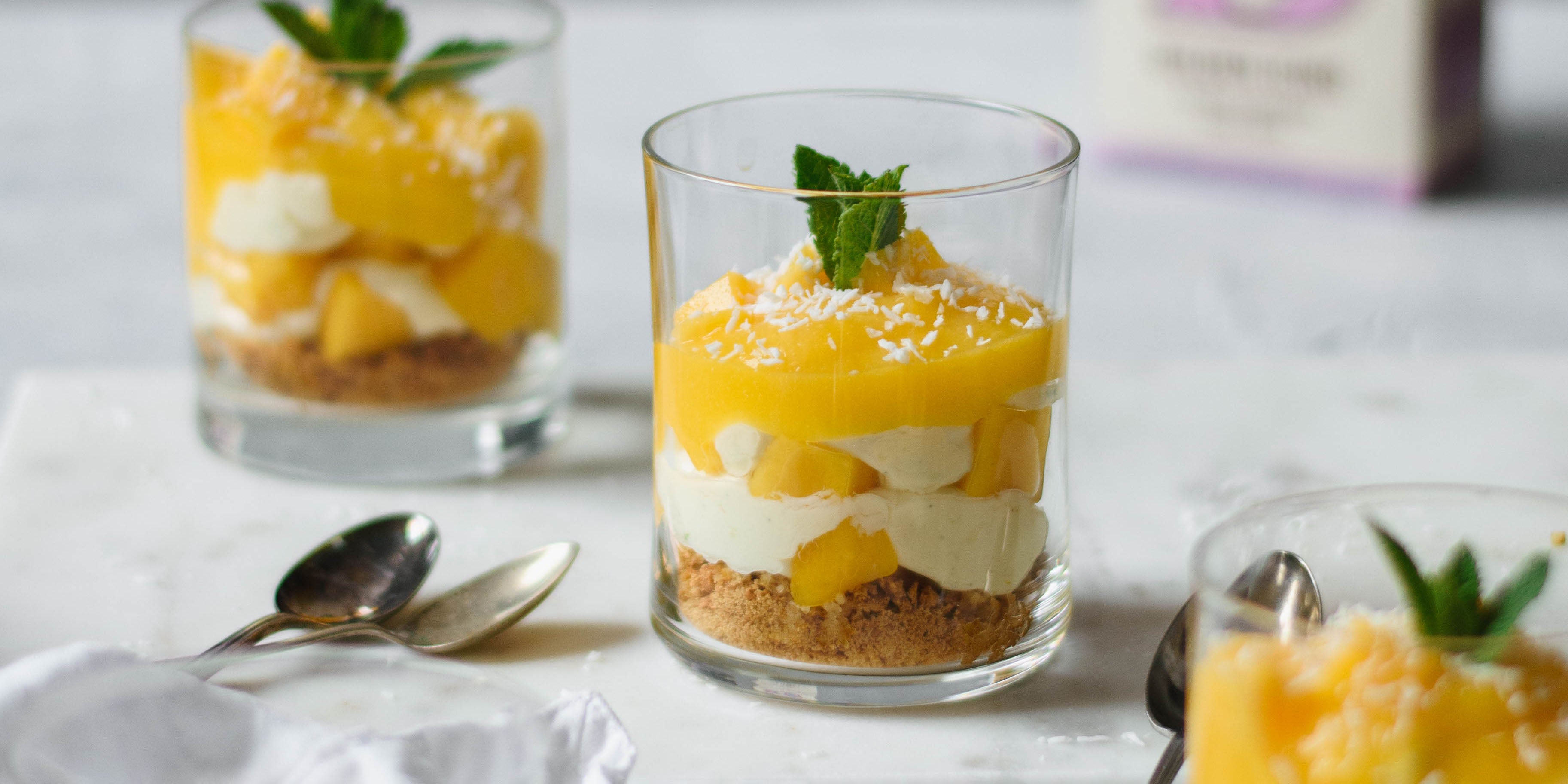 3 small glasses of mango syllabub with sprig of mint on top and two spoons