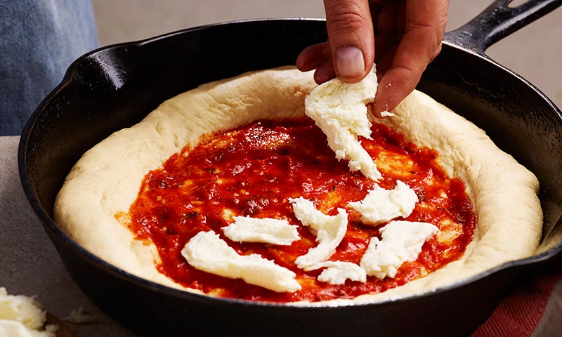 Adding pieces of mozzarella cheese to a Deep Pan Pizza