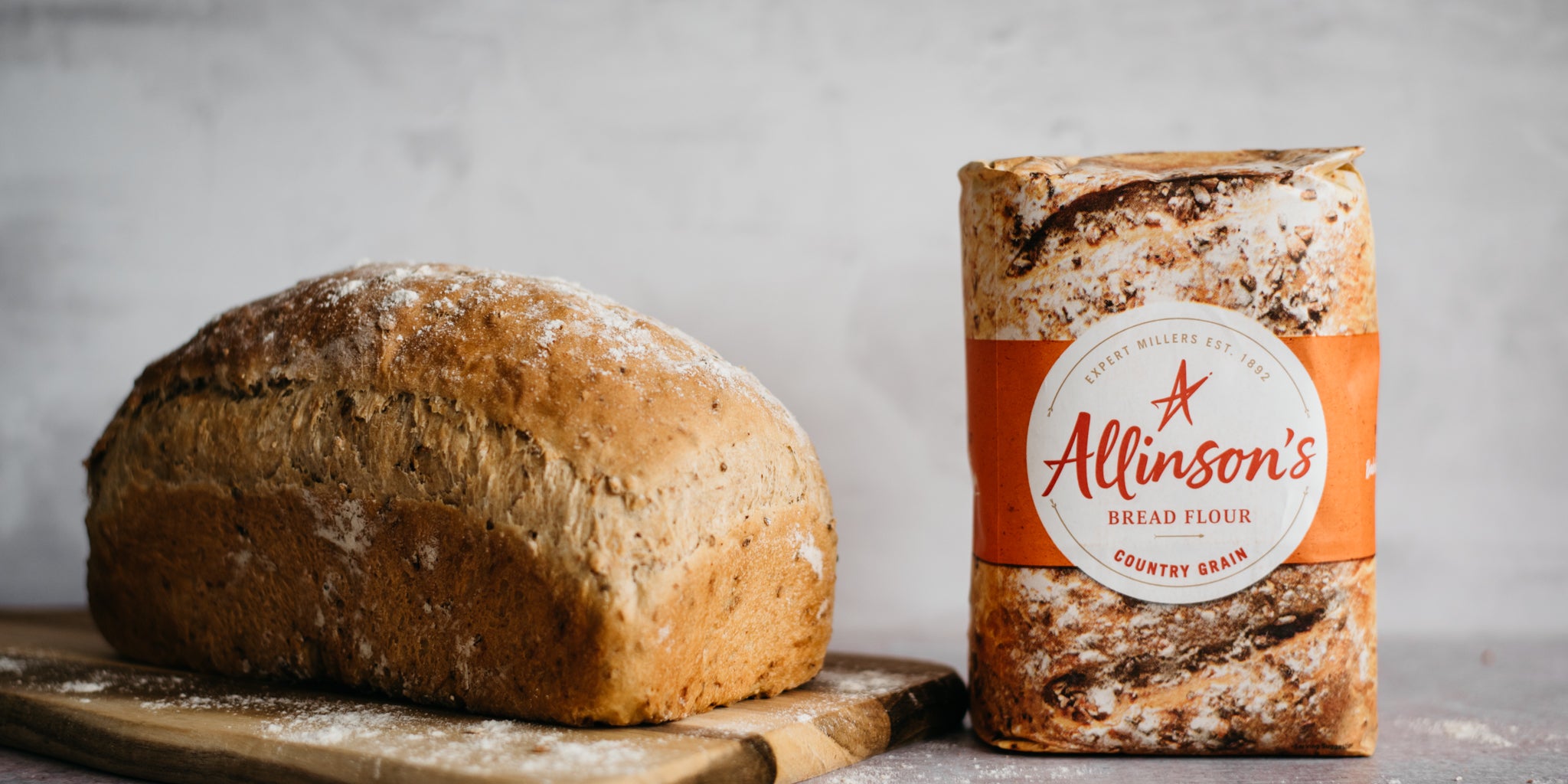 Farmhouse Country Grain Loaf on a serving board, dusted in flour next to a bag of Allinson's Country Grain Flour