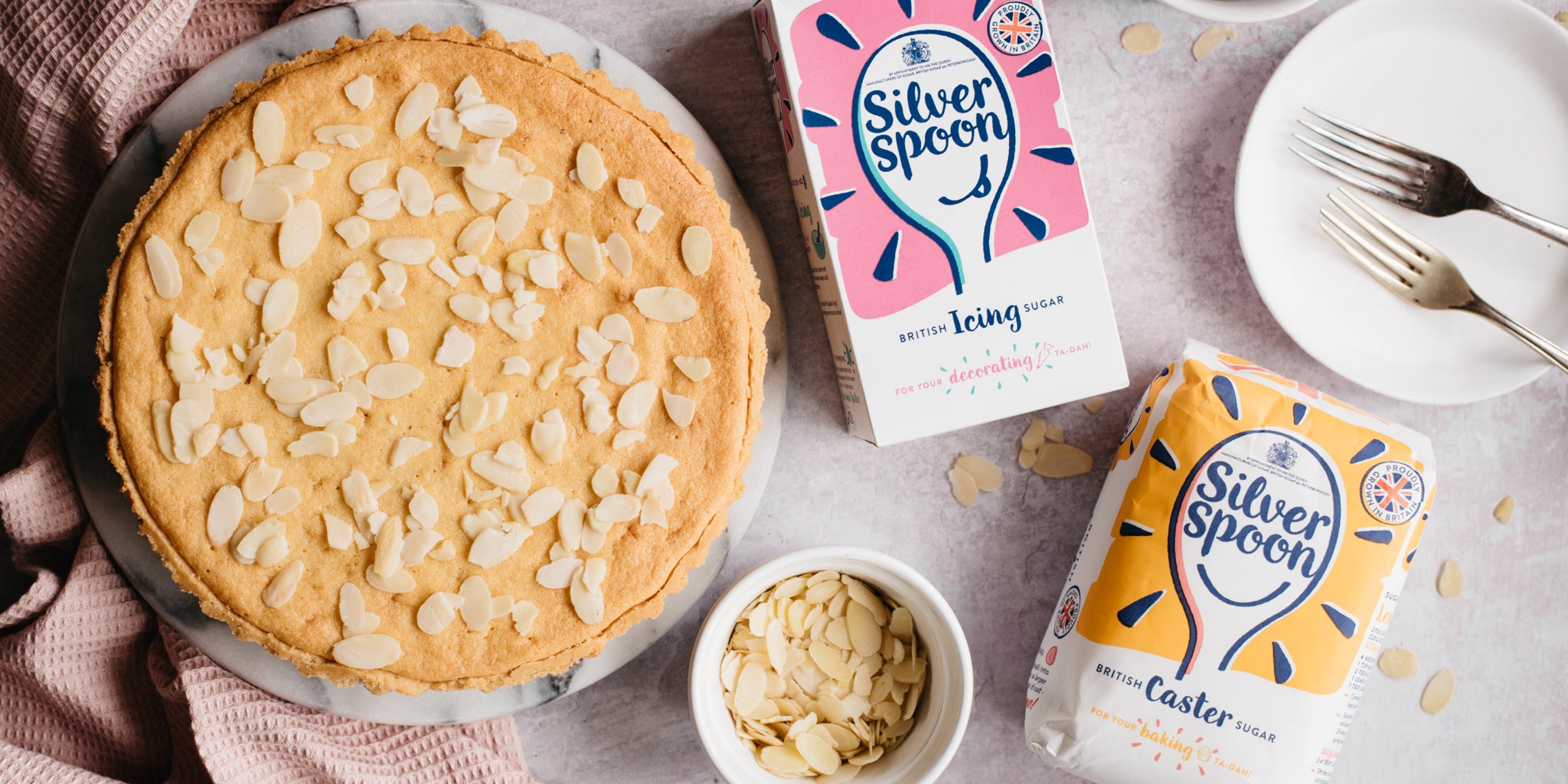 Top view of Simple Bakewell Tart scattered with almonds, next to a bag of Silver Spoon Icing and Caster Sugar