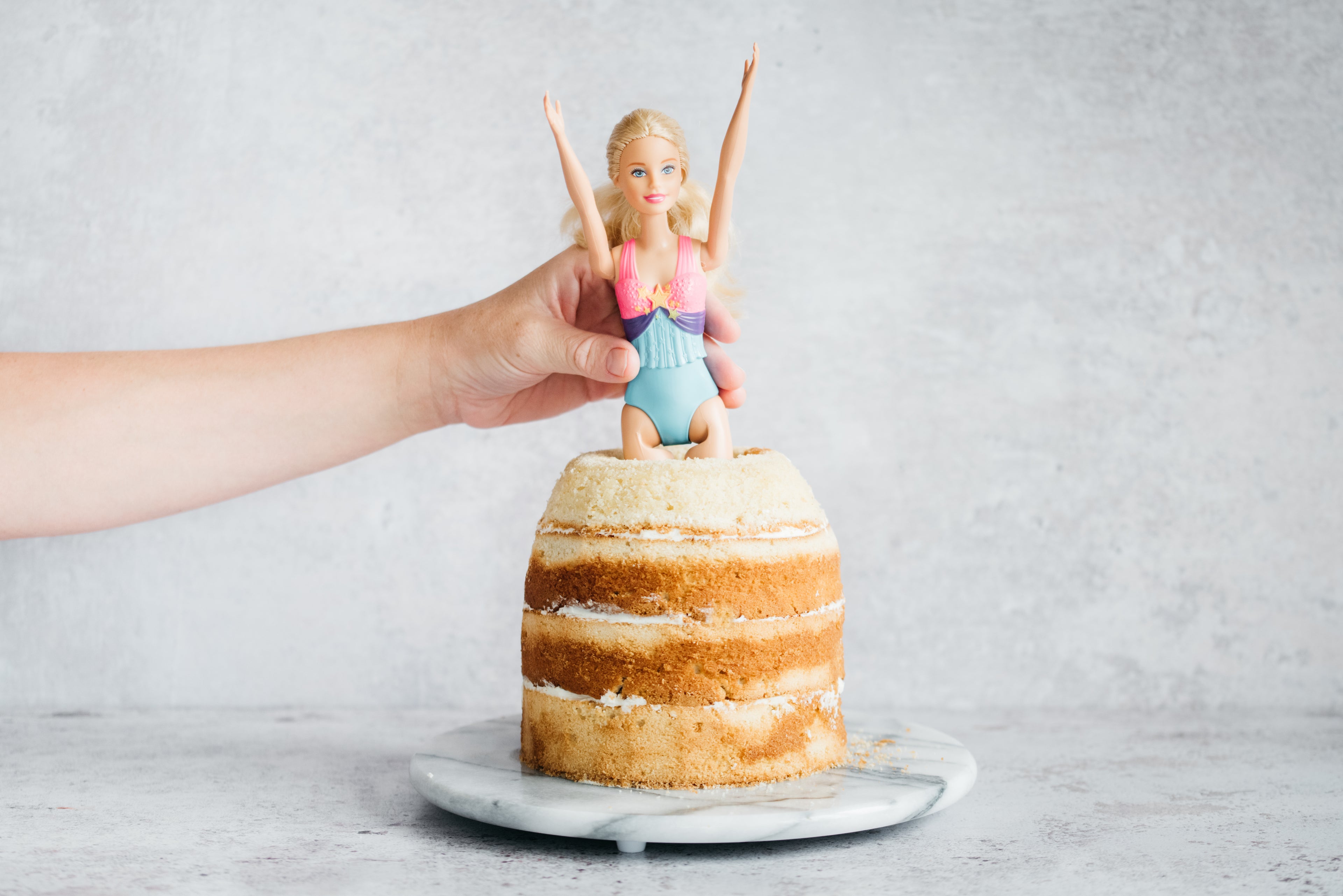 Princess Barbie Cake being built around a barbie doll in the centre of four layers of sponge cake