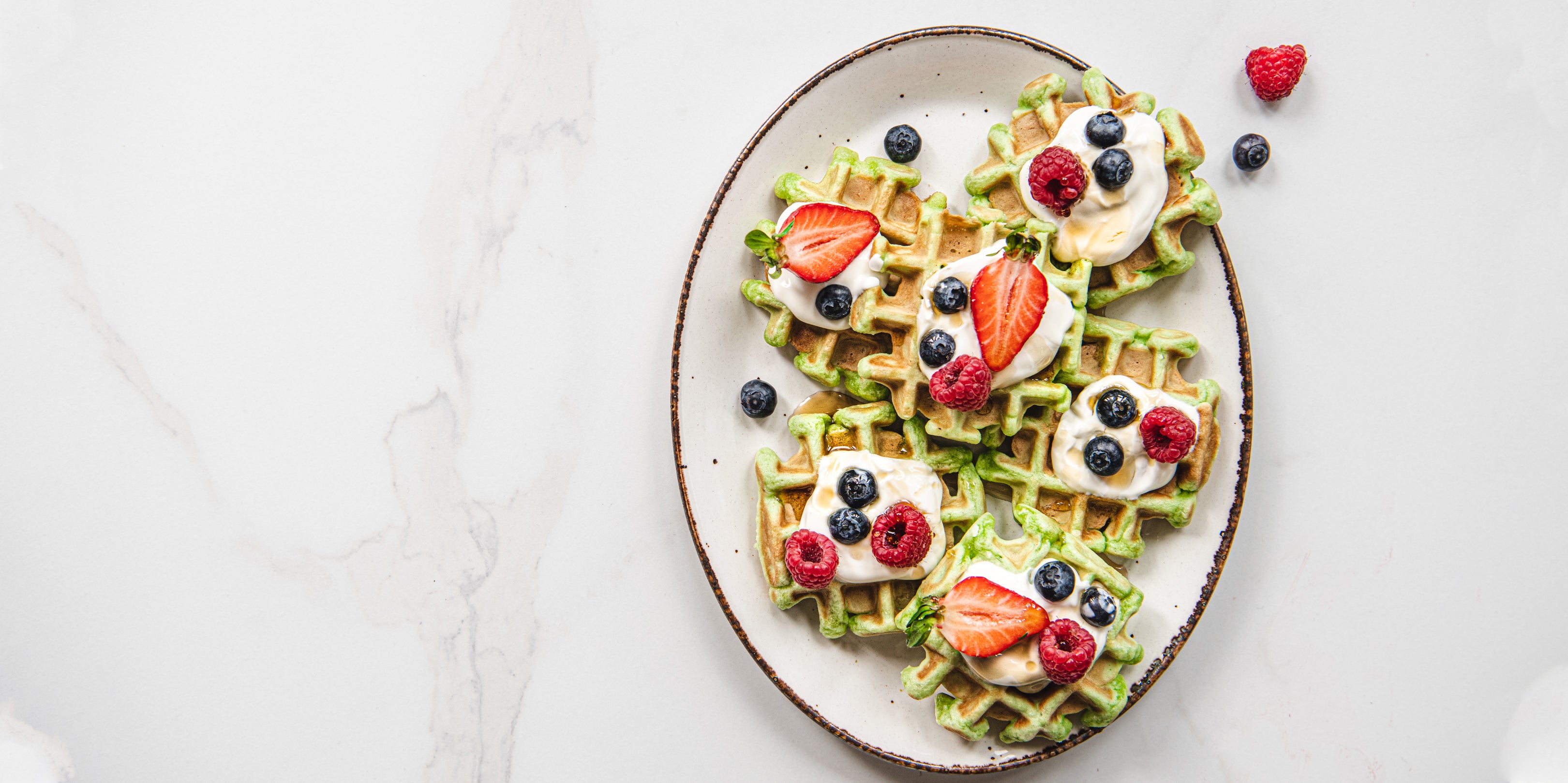 Pandan Waffles on a serving plate, sprinkled with fresh berries and dollops of yoghurt