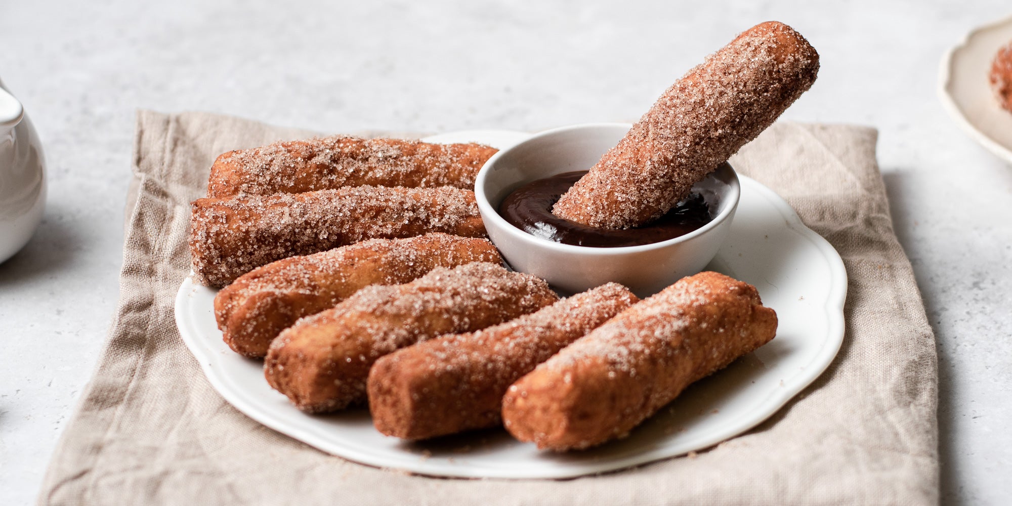 Doughnut Stick being dipped into chocolate dip surrounded by sugared doughnut sticks on a serving plate