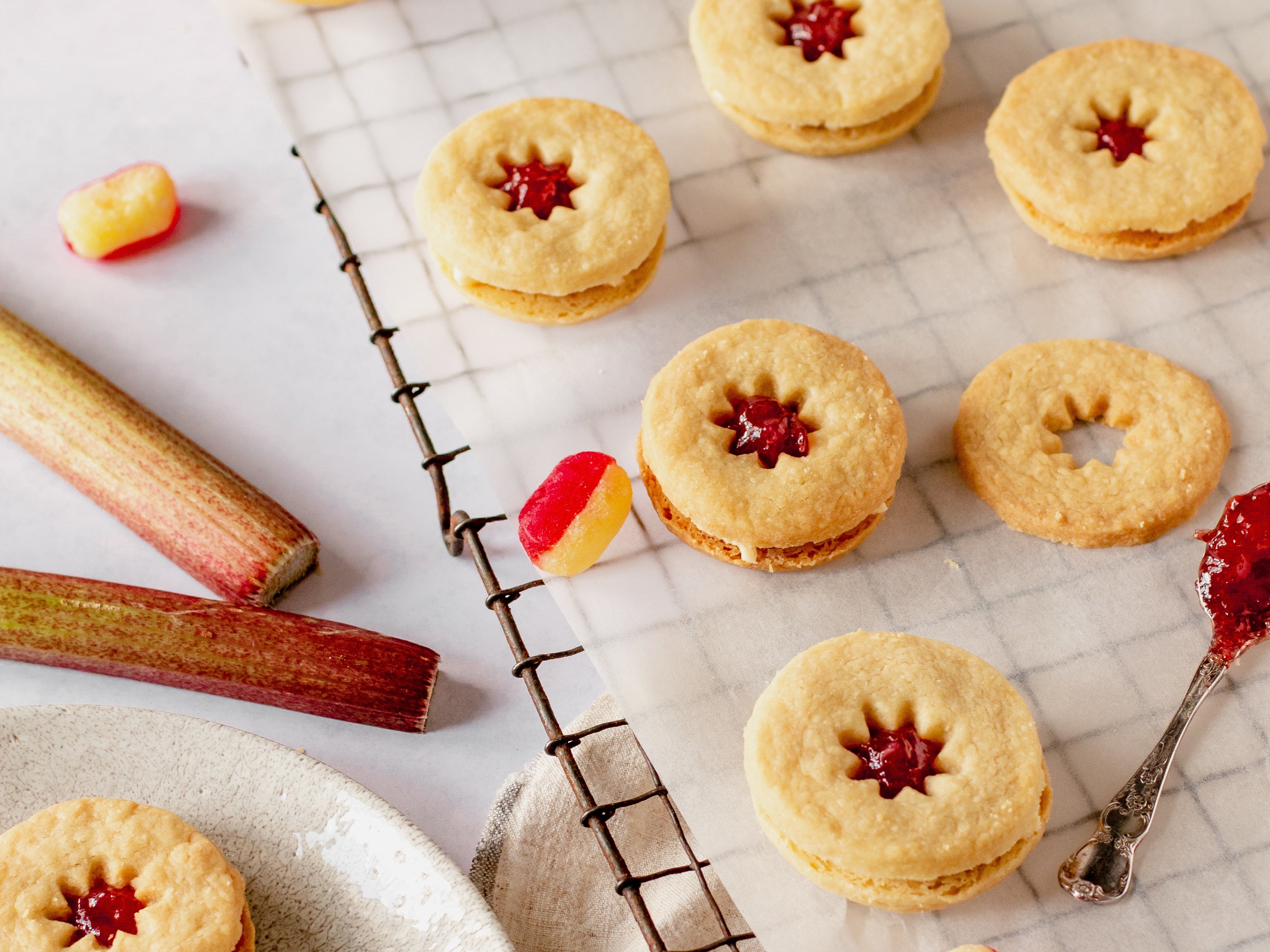 Jammy dodger biscuits on cooling rack with sweets, rhubarb sticks and jammy spoon