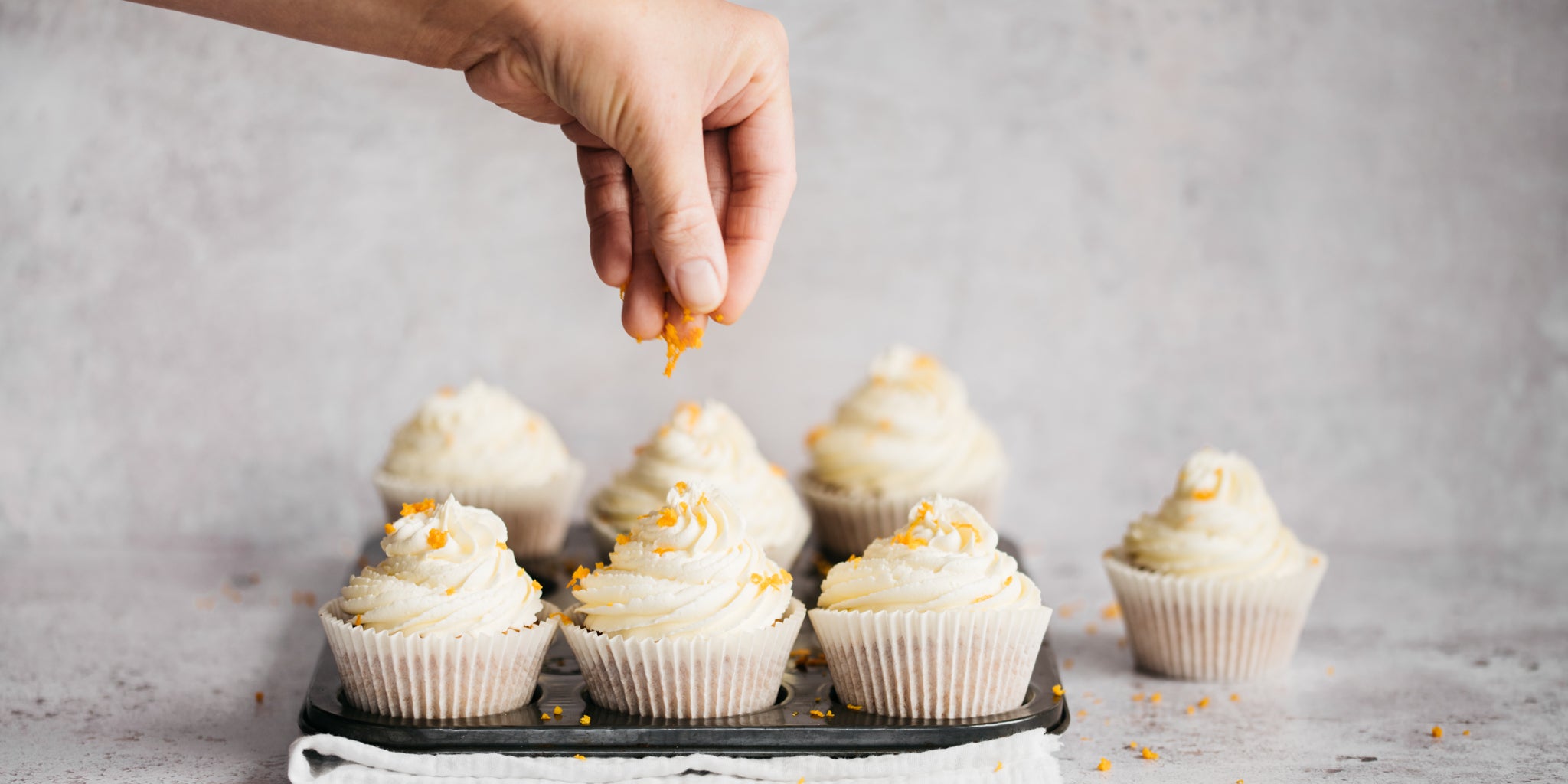 Orange Blossom Cupcakes being hand sprinkled with fresh orange zest