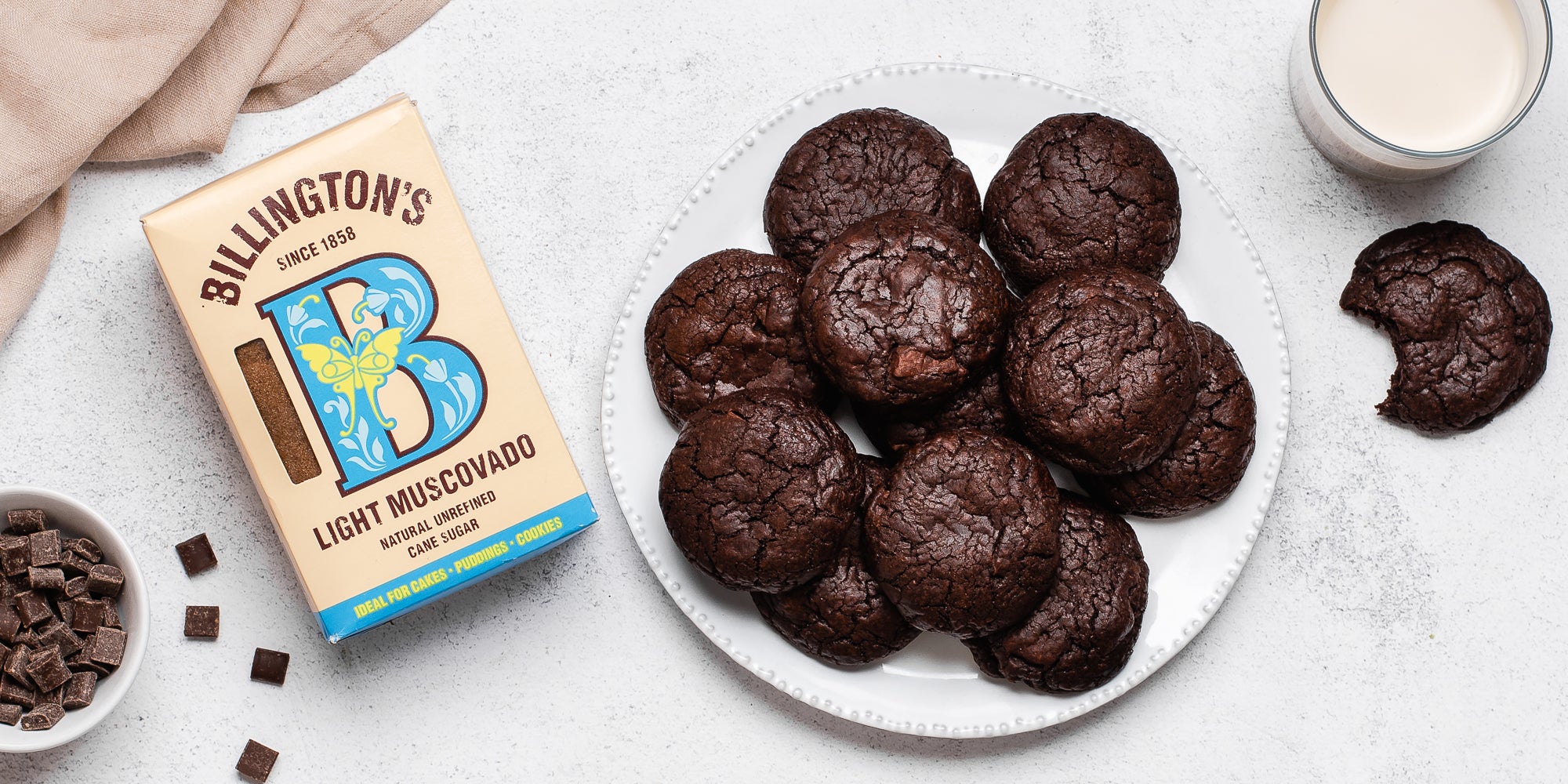 Chocolate Brownie Cookies on a plate next to a flat lay box of Billington's Light Muscovado sugar and a glass of milk