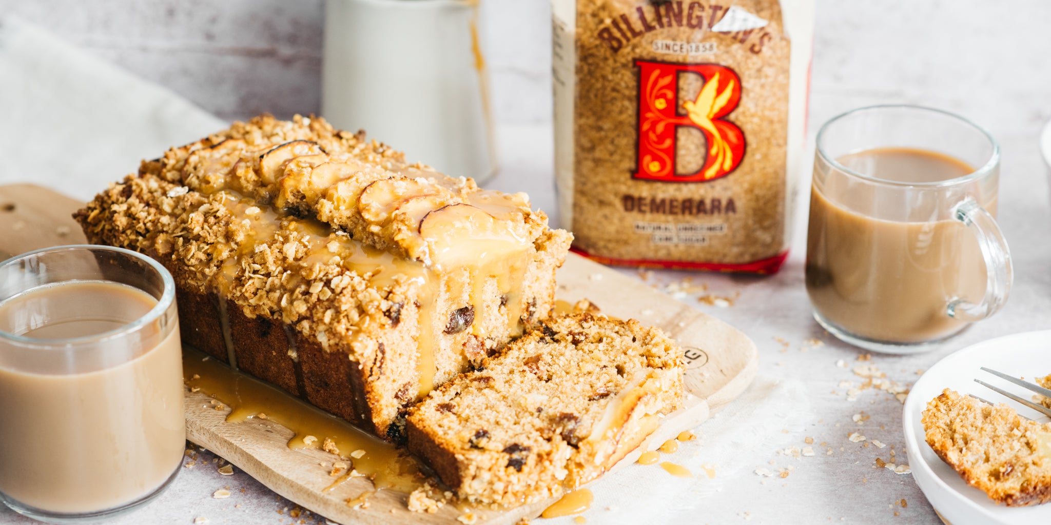 Apple cake sliced with cup of coffee beside and a demerara pack next to 