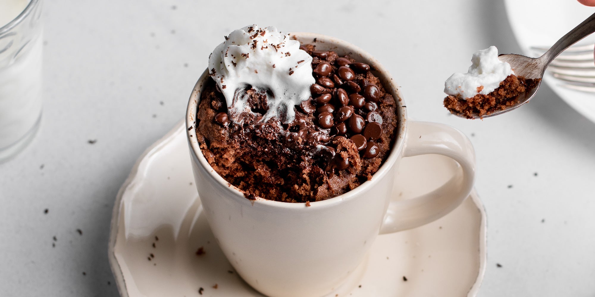 Close up of Chocolate & Peanut Butter Mug Cake with a spoon dipping into it. Melted cream and chocolate drops on top.