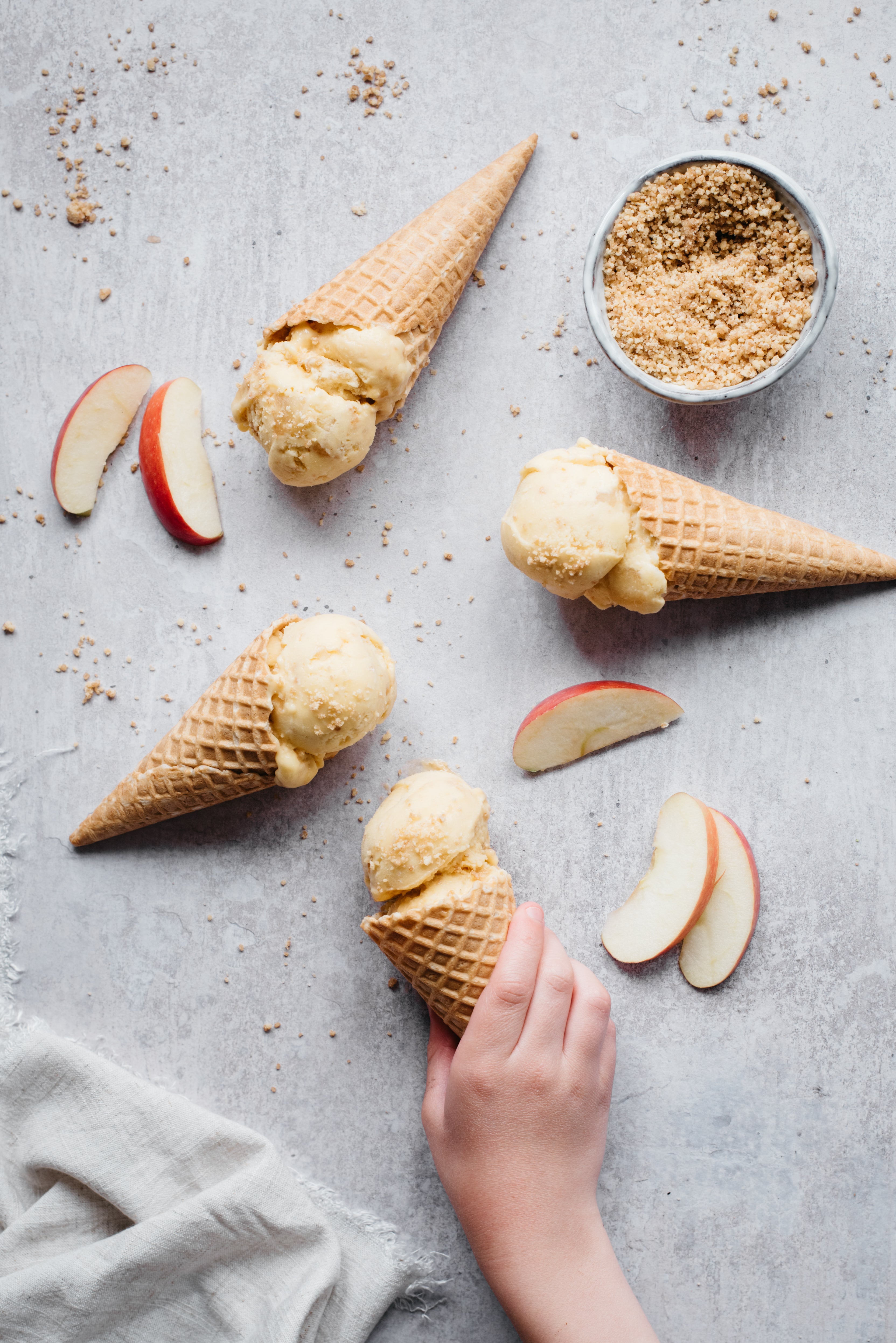 Scoops of homemade apple crumble ice cream in cones, surrounded by slices of apple