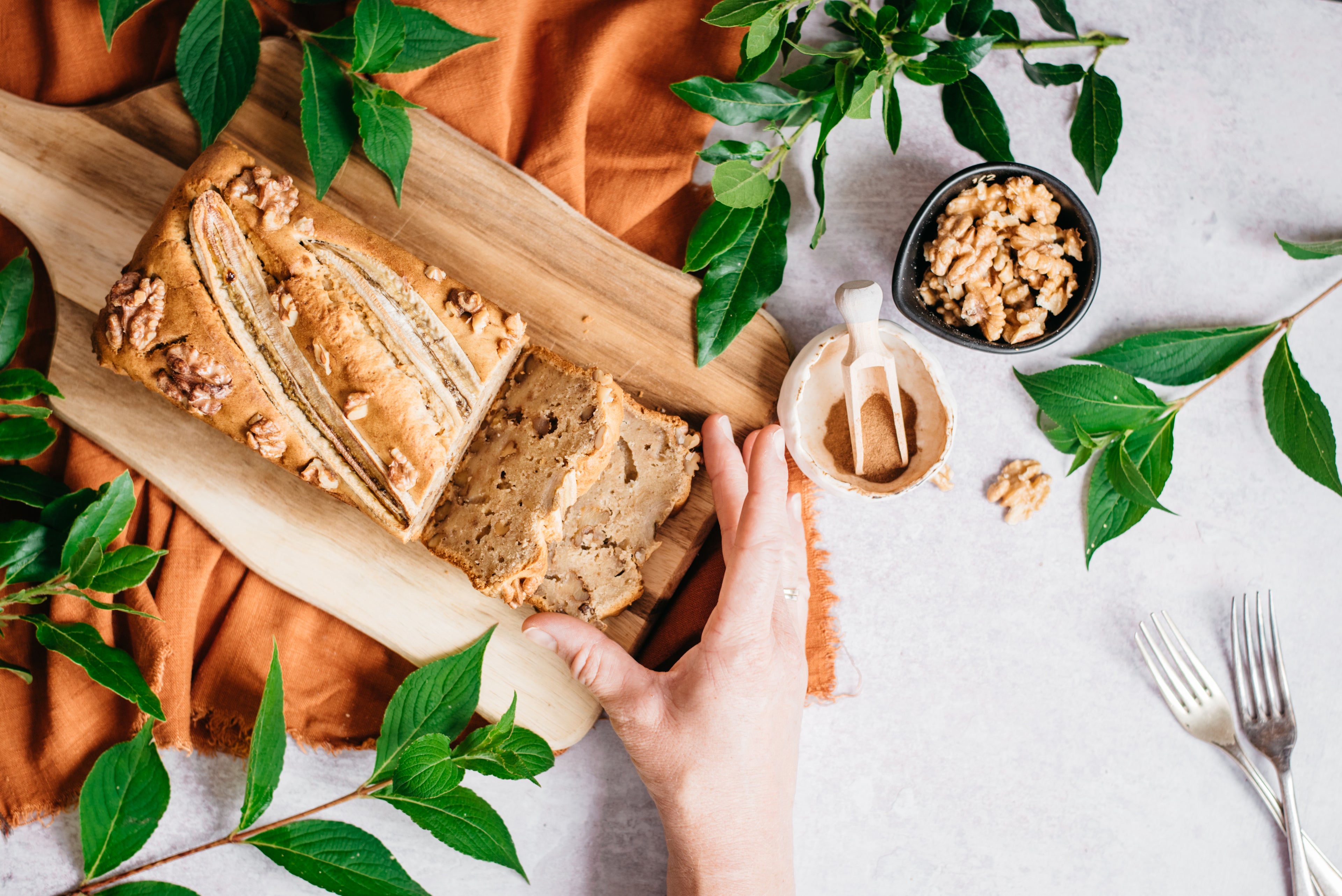 Top down view of a loaf of banana bread with a hand taking a slice away